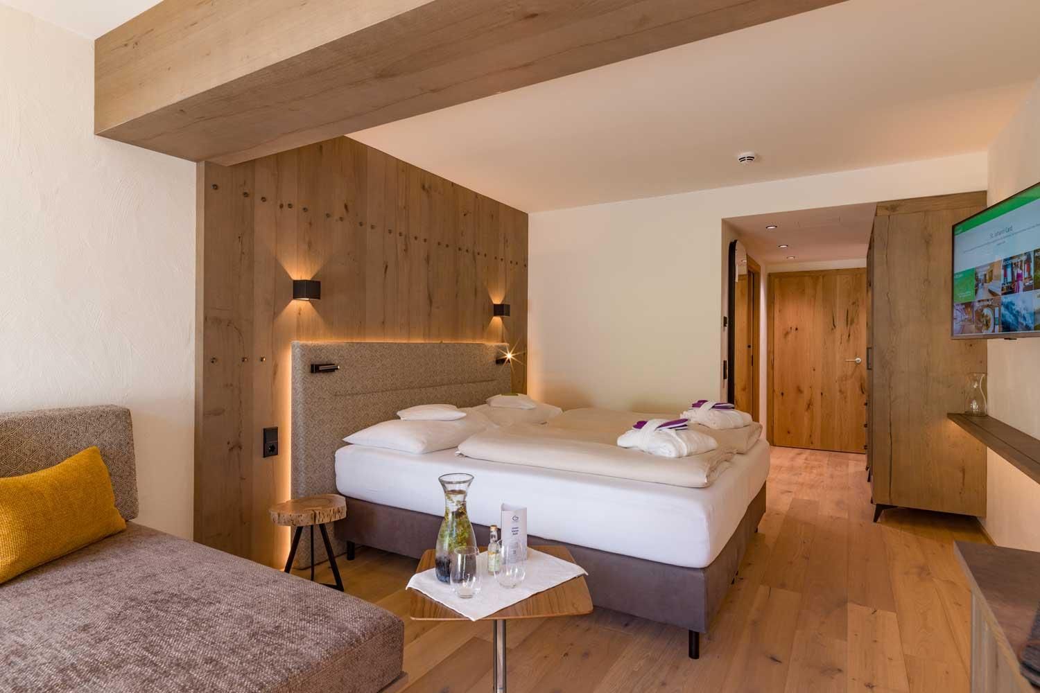 A modern room with wooden paneling and a large bed. There is a cozy seating area and a flat-screen TV on the wall.