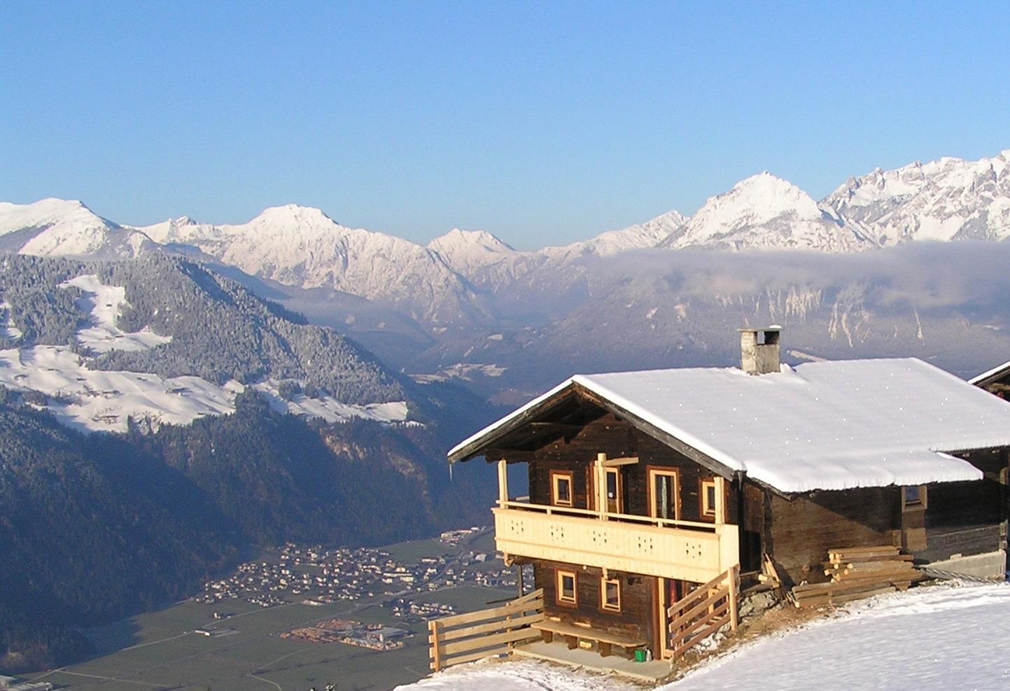 A picturesque mountain cabin in the snow-covered Alps. Majestic mountains rise in the background under a clear blue sky.