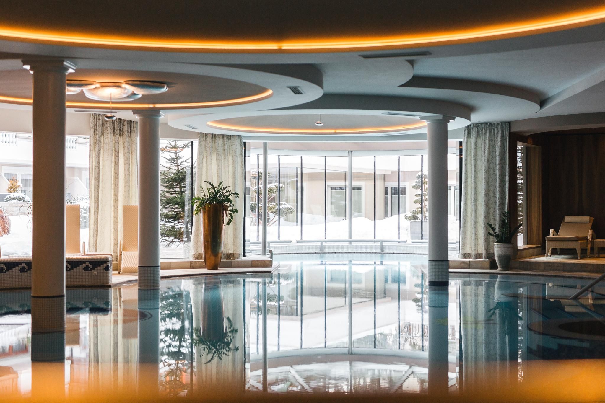 An elegant wellness area with an indoor pool and large windows. The atmosphere is relaxed and inviting, surrounded by snow and plants.