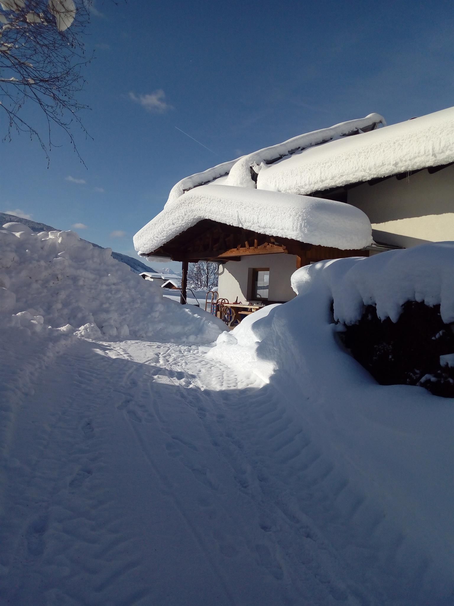 A snow-covered path leads to a building with a snow-covered roof. The clear blue sky is visible in the background.