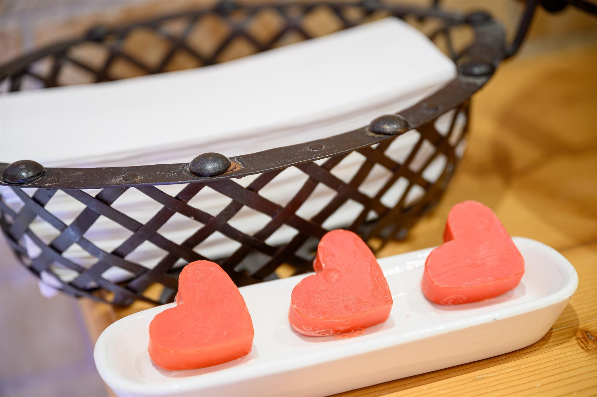 A basket with a white towel and three heart-shaped, red soaps on a white plate. The soaps are arranged decoratively and lend a romantic atmosphere.