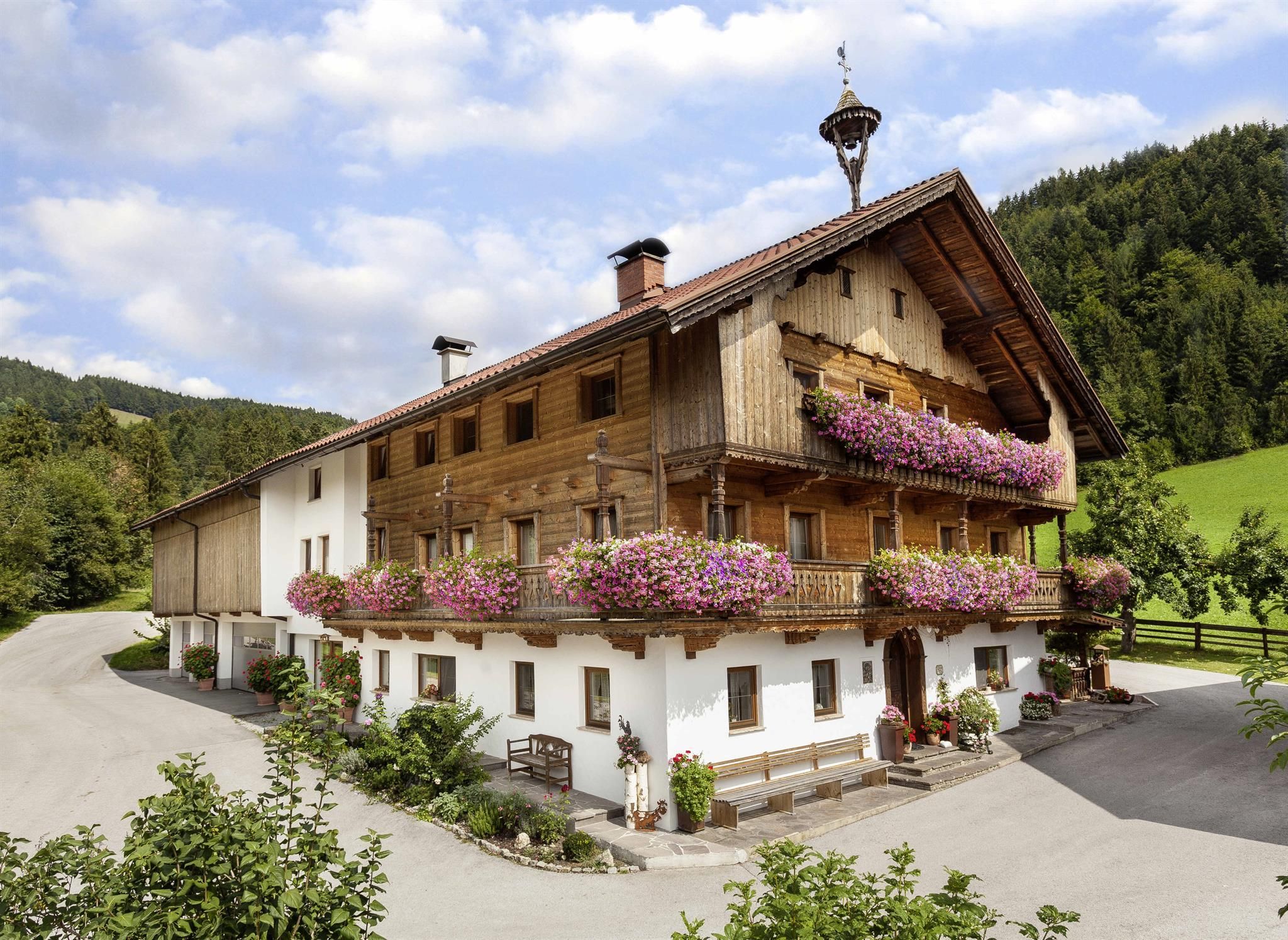 A traditional wooden house with colorful flowers on the balconies. Surrounded by green meadows and mountains.