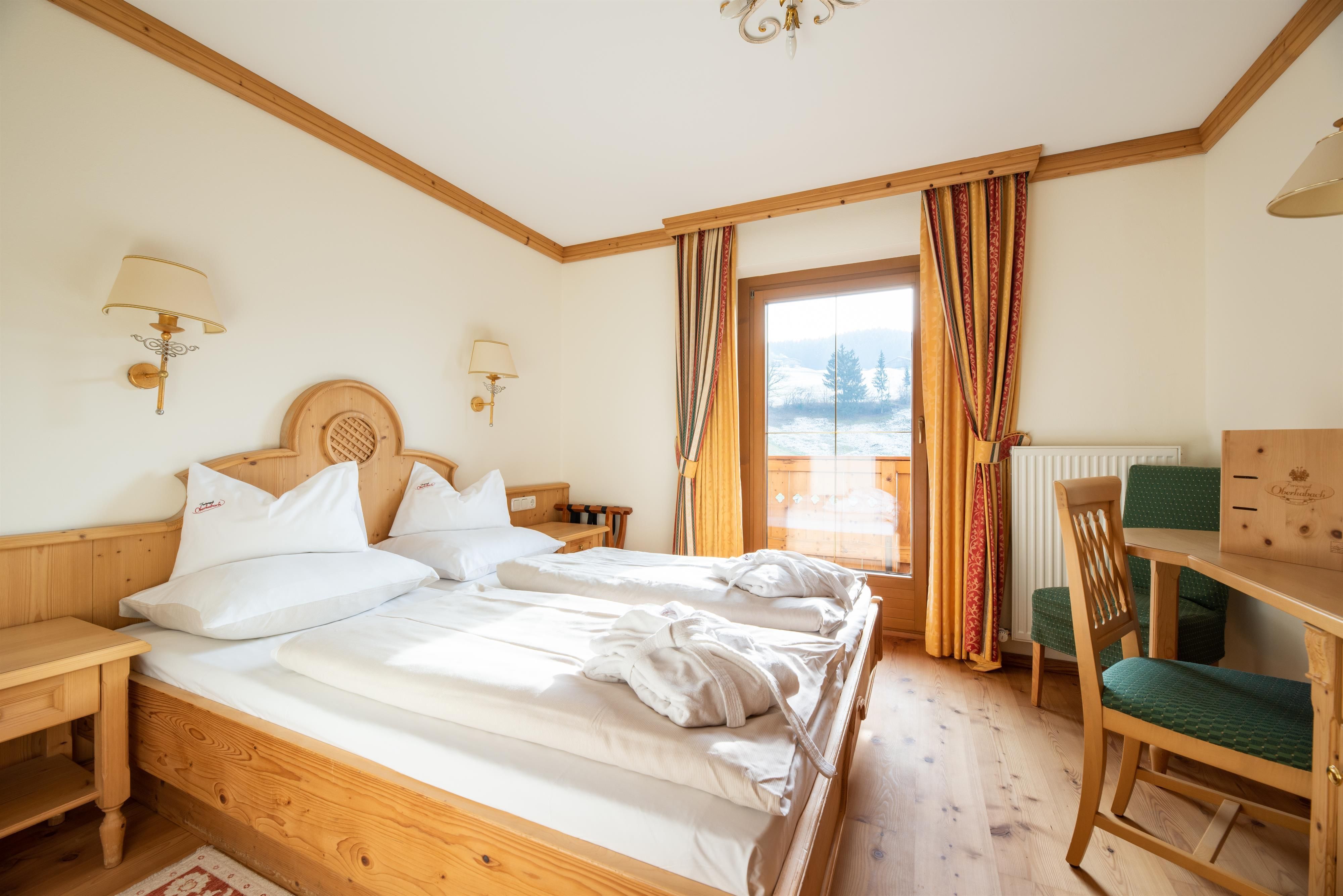 A cozy room with two single beds and wooden details. The large window front provides access to a balcony and plenty of daylight.