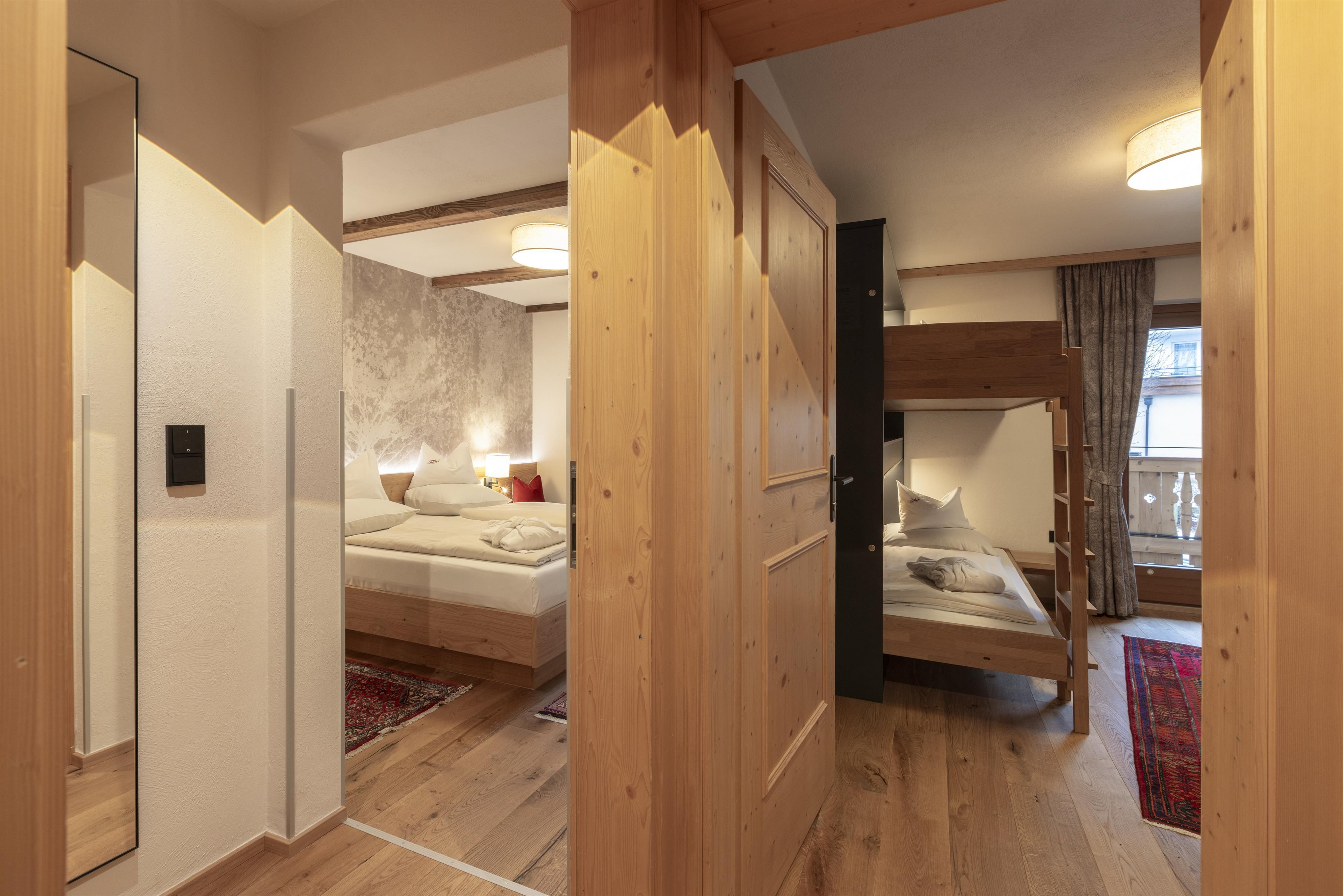 A cozy hallway with wood paneling that leads to two bedrooms. The rooms contain beds and natural light filtering through the windows.
