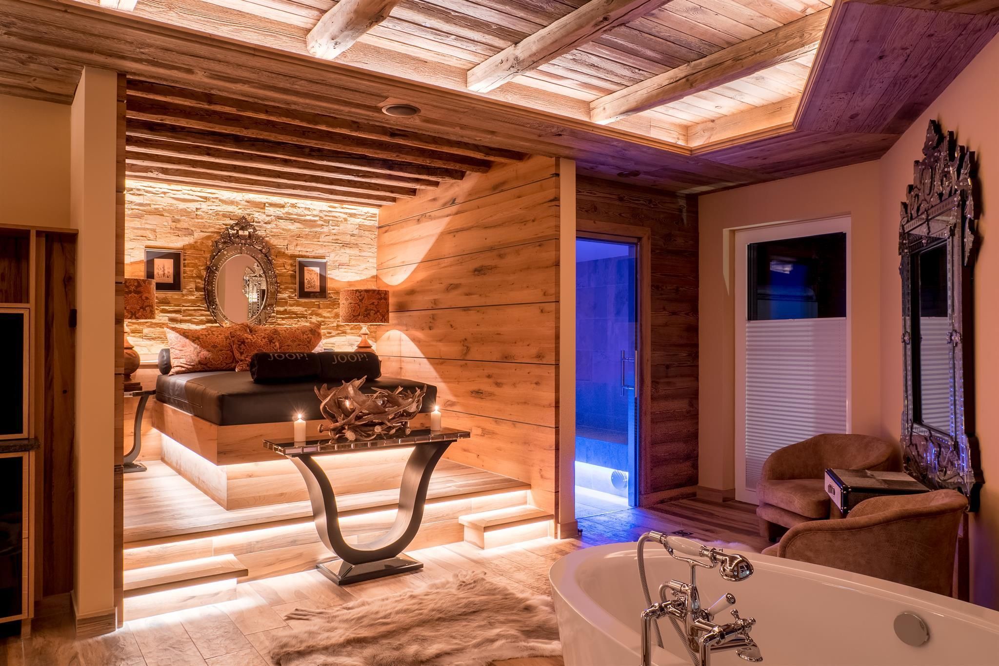 An elegant and modern bedroom with wooden paneling and soft lighting. On the left side, there is a bathtub and a cozy sitting area.