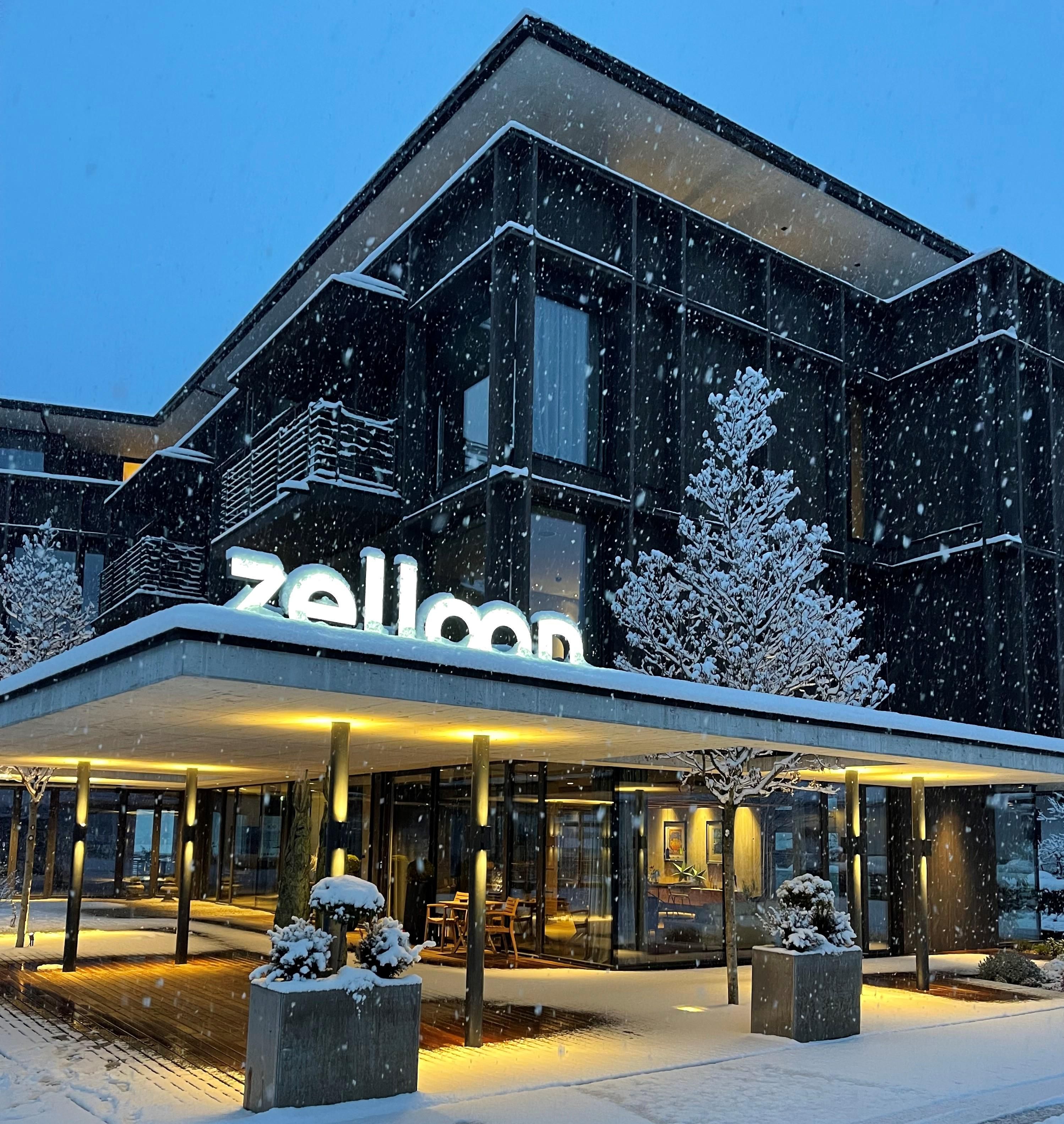 A modern hotel building in the snow with a glowing sign. Gentle snowflakes are falling and the surroundings are winterly quiet.