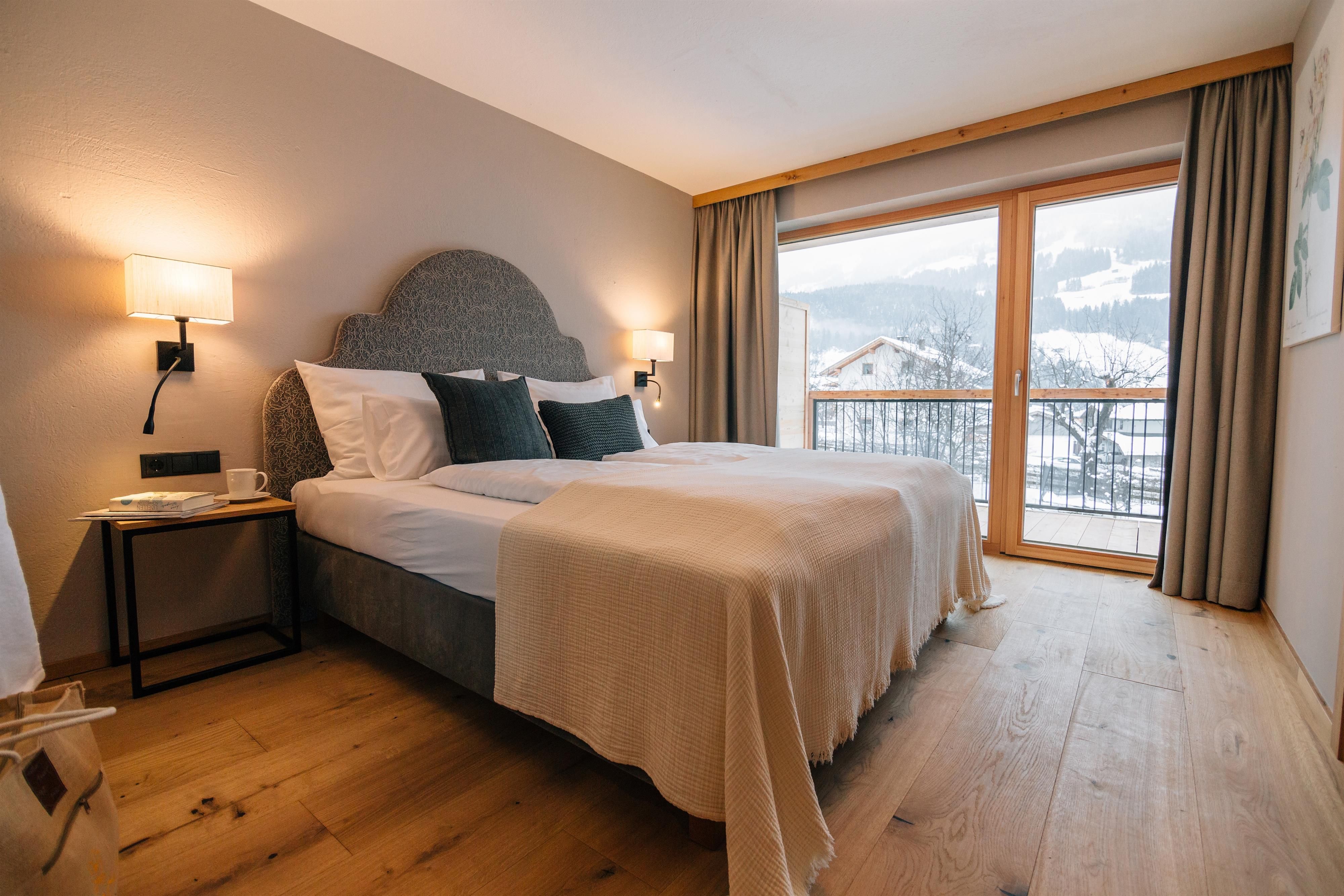 A modern bedroom with a large bed and stylish pillows. The room has a window overlooking the mountains and plenty of natural light.
