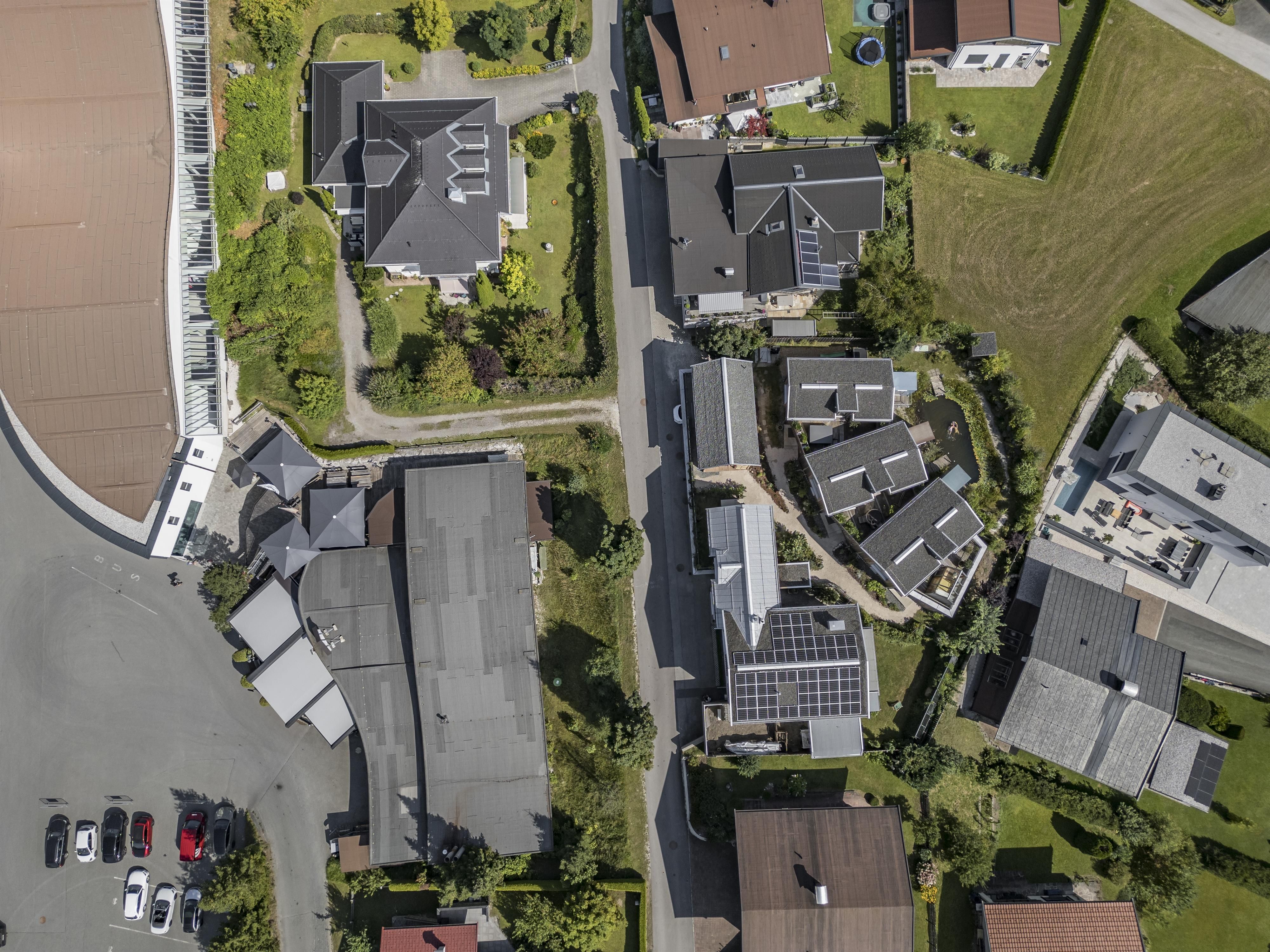 An airy view of a residential area with several houses and gardens. The streets are clearly visible and vehicles are parked in a parking lot.
