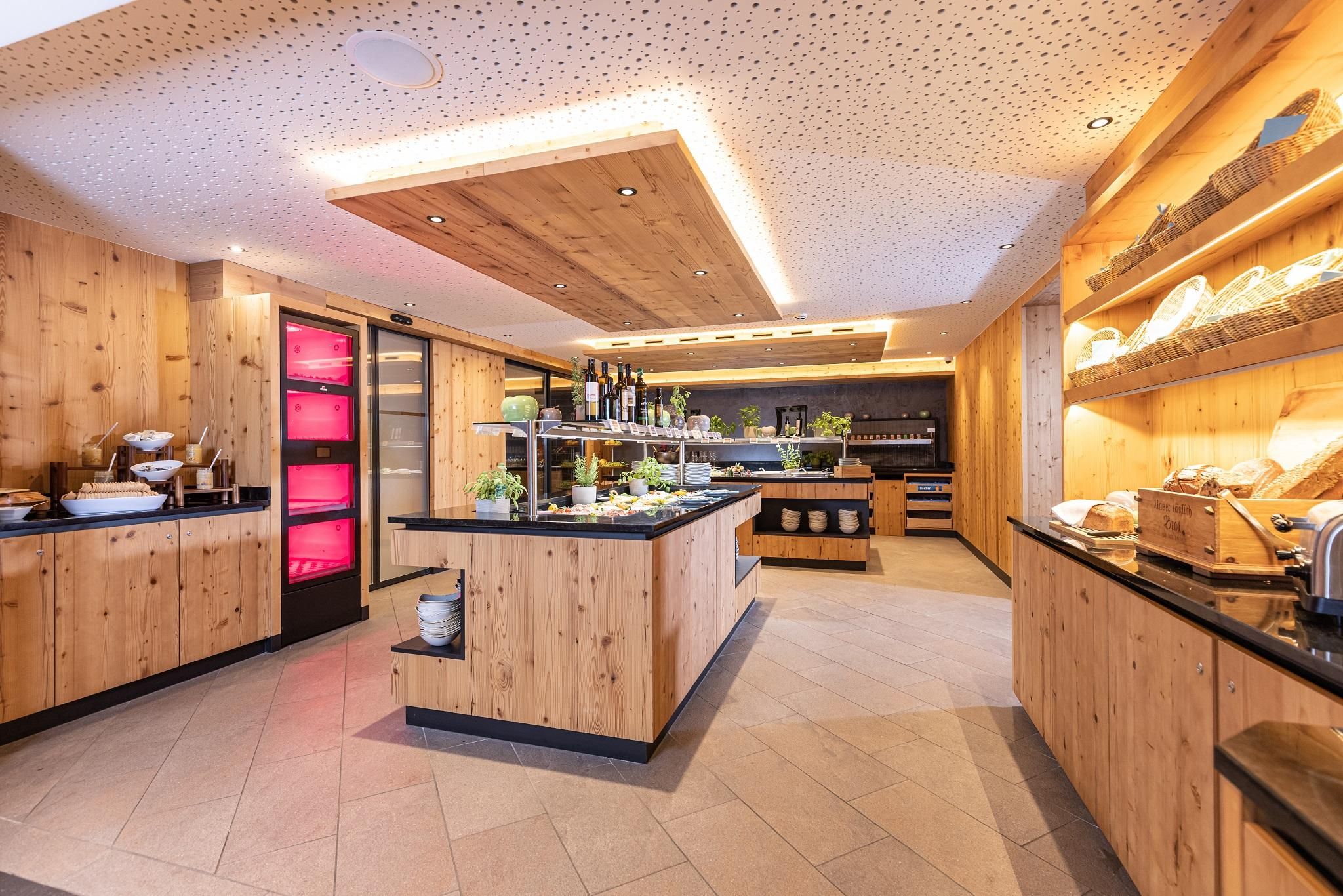 A stylish interior with a wood design. There is a central counter with various food items and a refrigerator in the background.