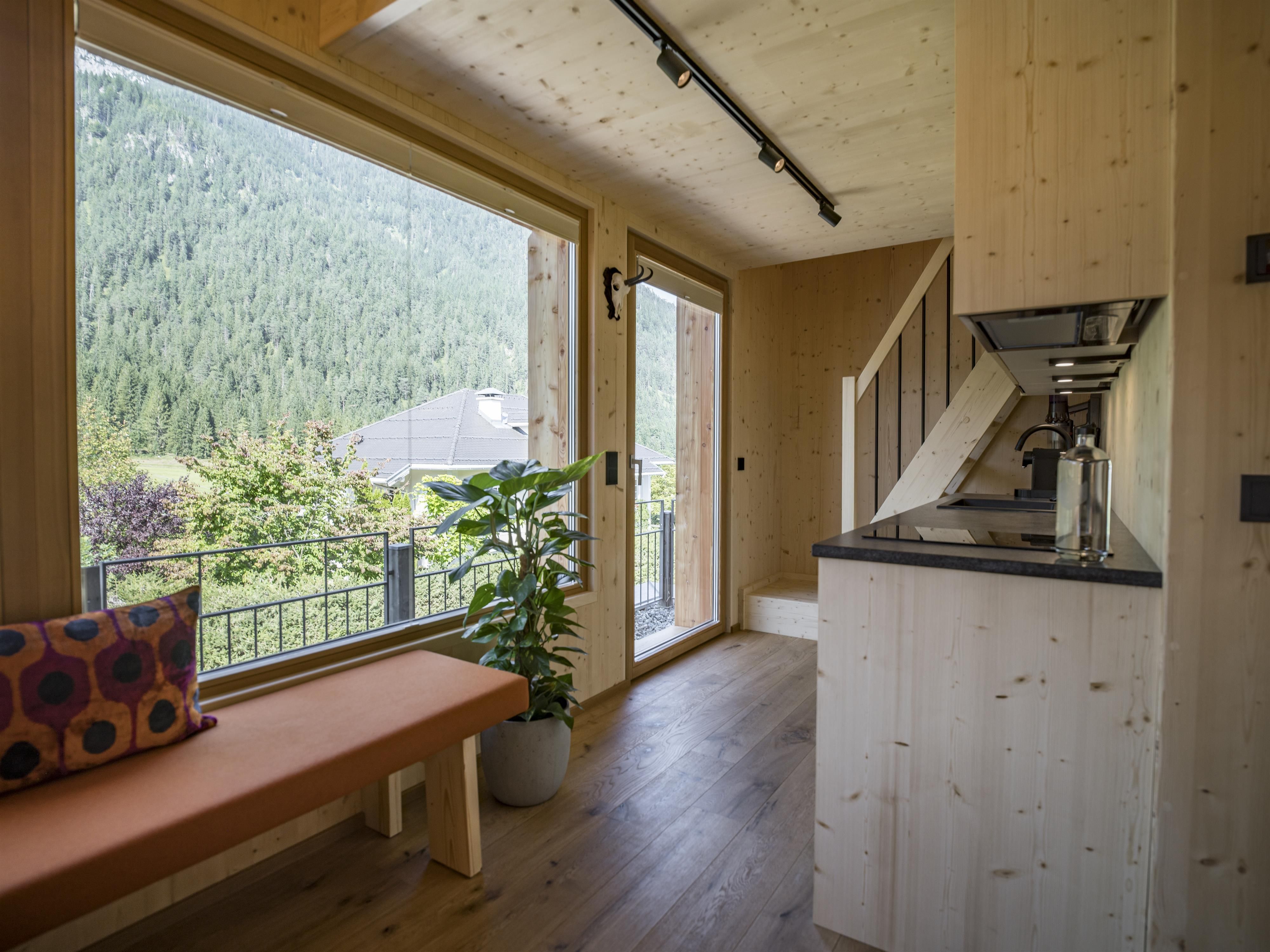 A cozy wooden apartment with a modern kitchen and large windows. In the background, green mountains are visible.