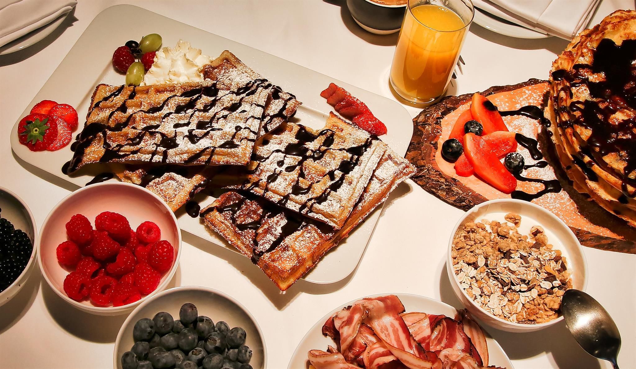A hearty breakfast with waffles, fresh fruit, and chocolate. There's also yogurt, muesli, and fresh juice.