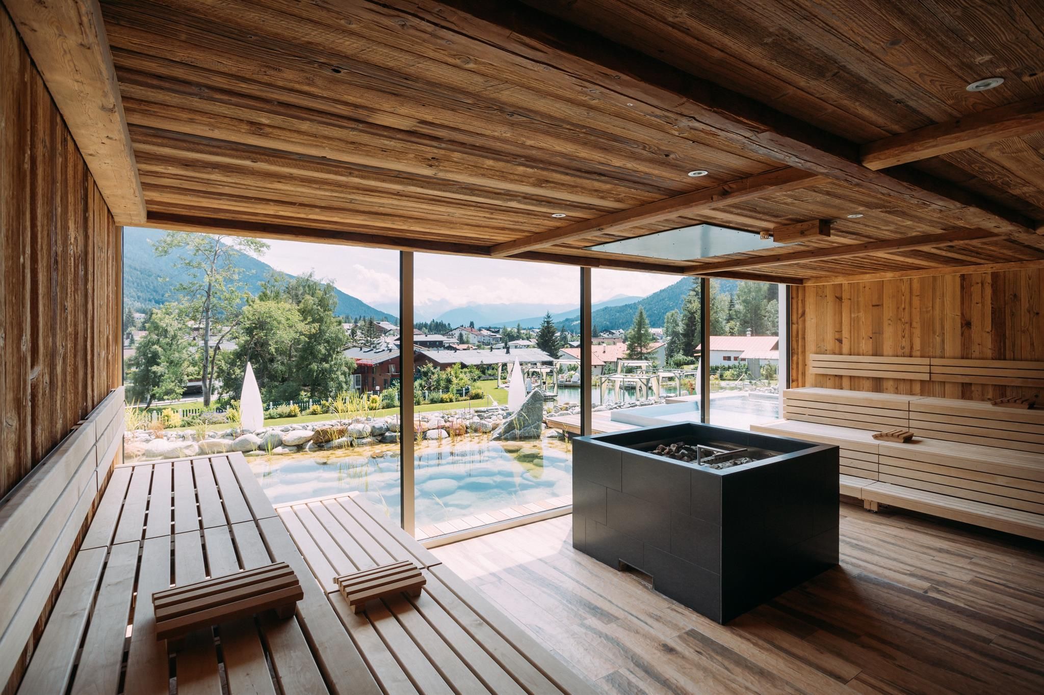 A modern wellness area with wood paneling and large windows. In the background, mountains and a pool are visible.