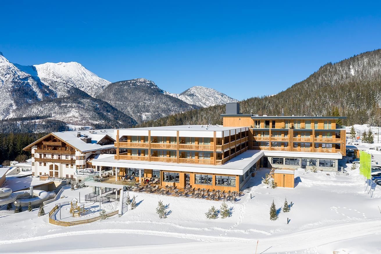 A modern hotel in the mountains, surrounded by snow and towering peaks. The sun shines brightly on the stunning landscape.