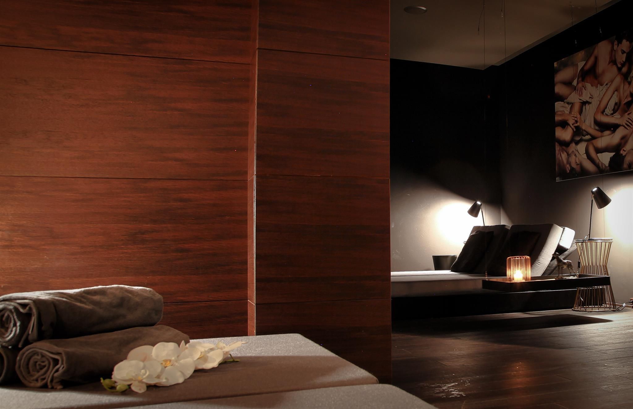A relaxing wellness area with wooden accents and soft lighting. On the lounging area, there are some towels and a flower.