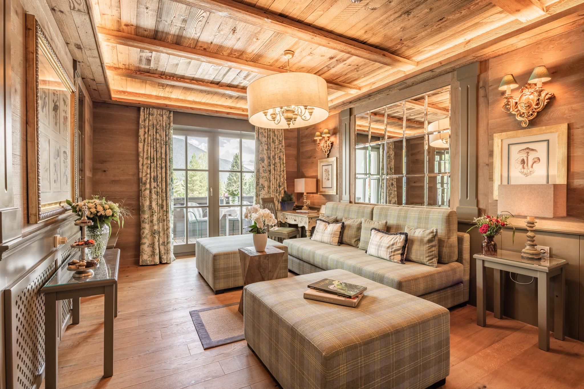A cozy living room with wooden paneling and a large window. The room is furnished with a comfortable sofa, an ottoman, and decorative elements.