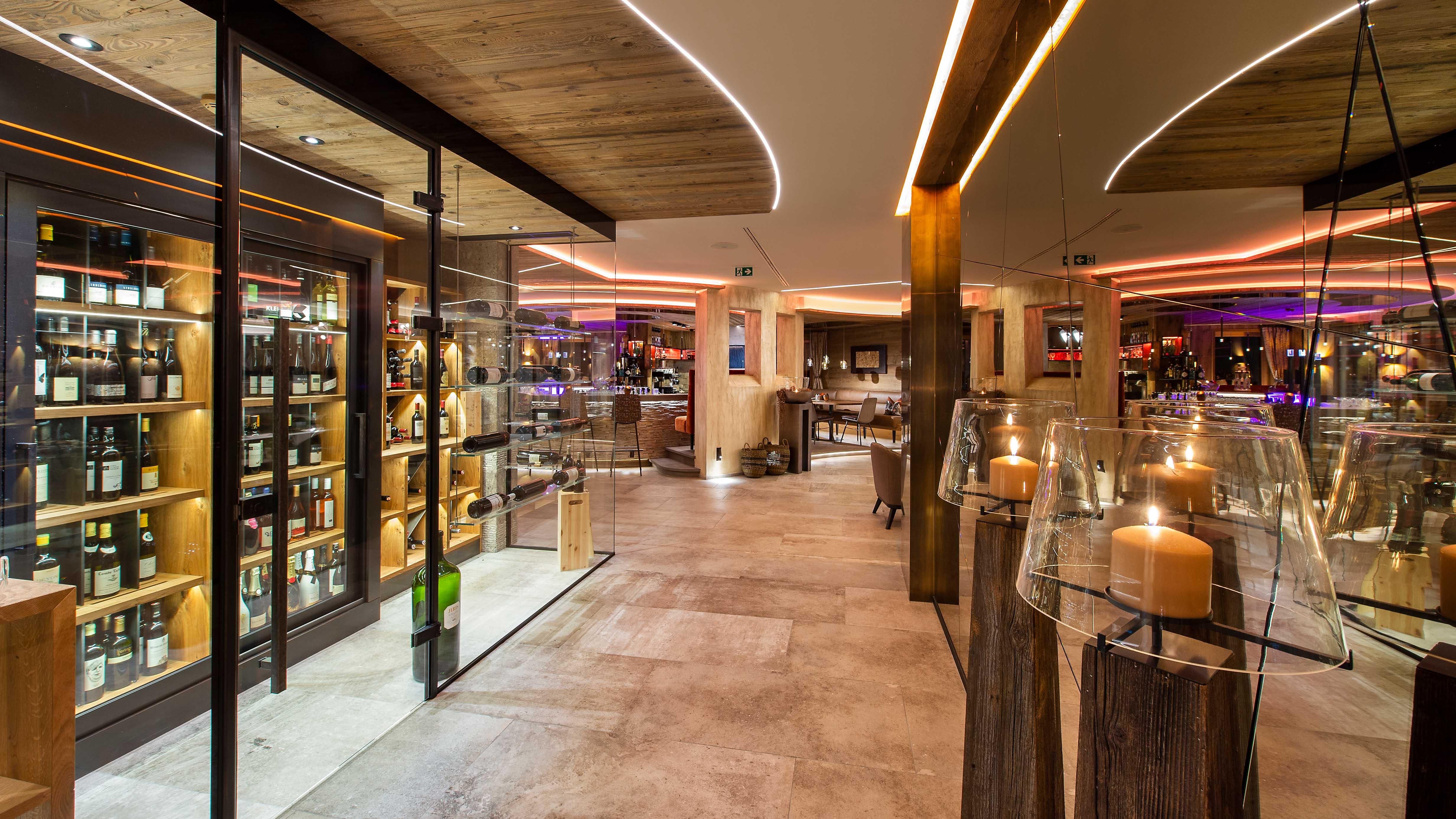 A modern bar with elegant lighting and wooden details. The walls are filled with shelves displaying various drinks.