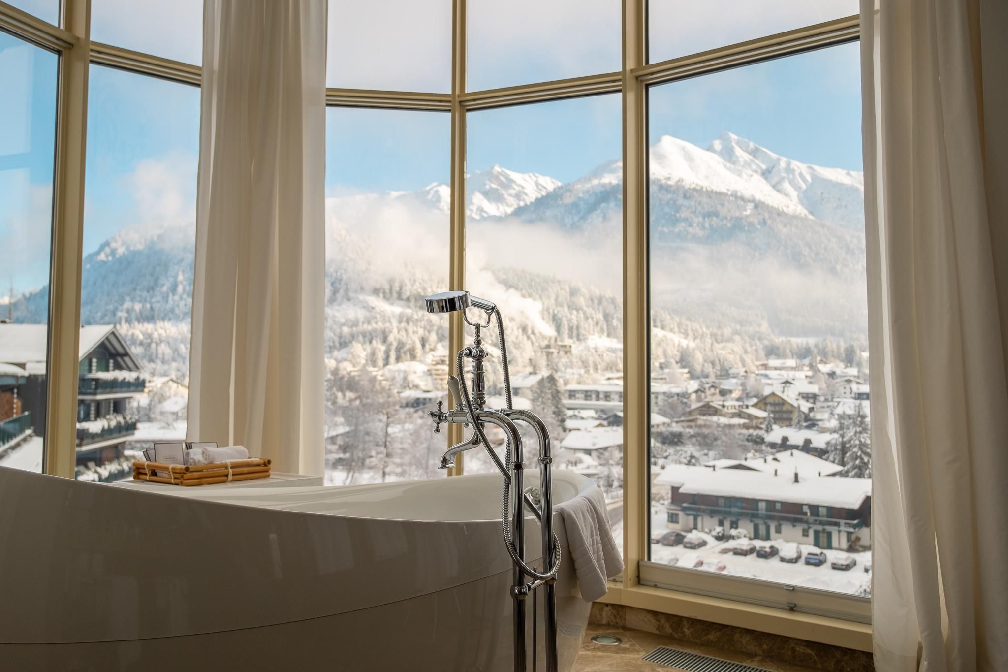 A modern bathroom with a bathtub and large windows. From there, one has a splendid view of snow-capped mountains and the surrounding landscape.