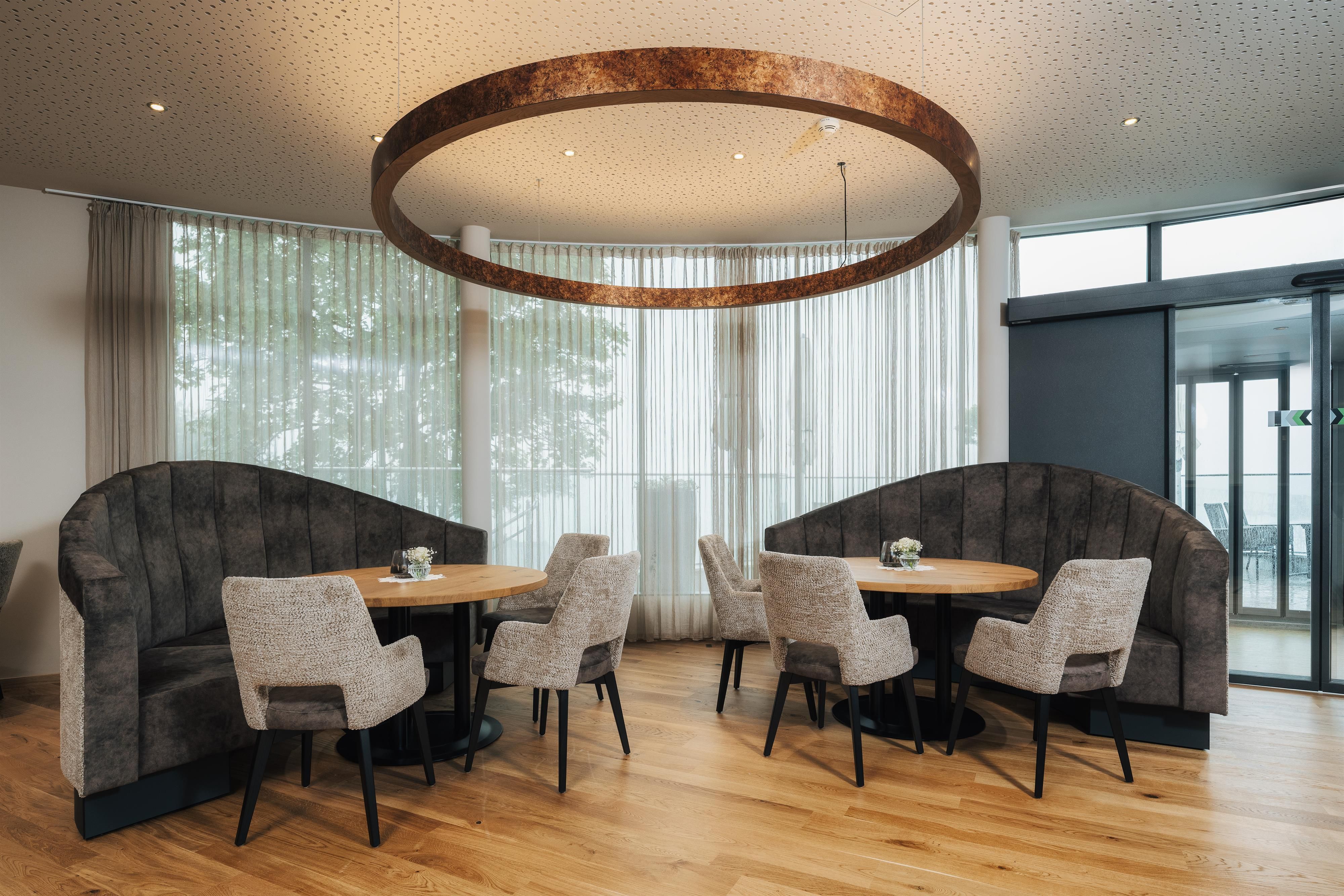 A modern restaurant with round wooden tables and upholstered chairs.
Large windows provide plenty of light and a view of the surroundings.