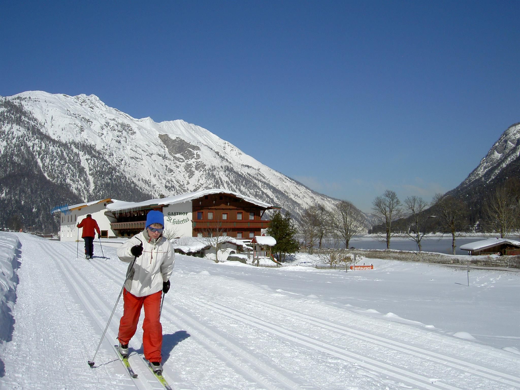 A snowy landscape with cross-country ski trails and tall mountains. Two skiers enjoy the winter scenery.