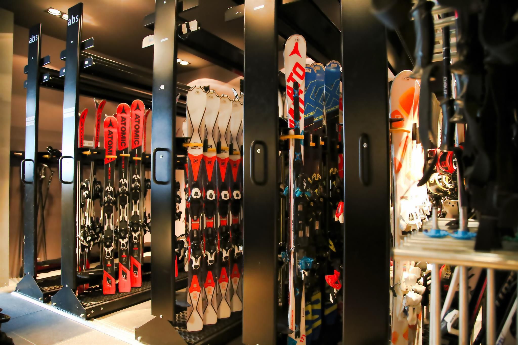 A ski room with several skis, neatly arranged in special holders. The walls are dark, which makes the colors of the skis stand out.