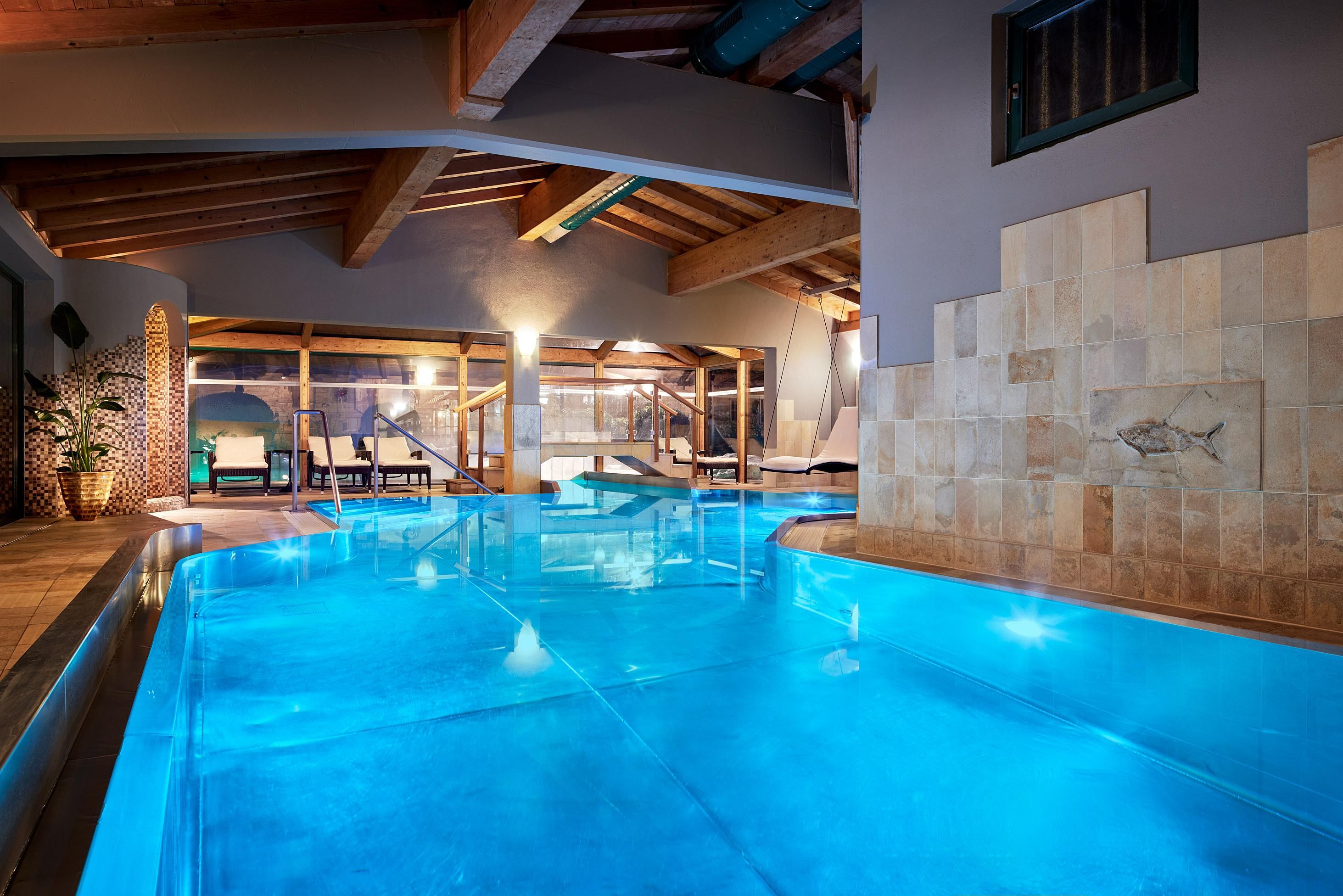 An elegant indoor pool with clear, blue water. The cozy atmosphere is enhanced by wooden paneling and decorative elements.