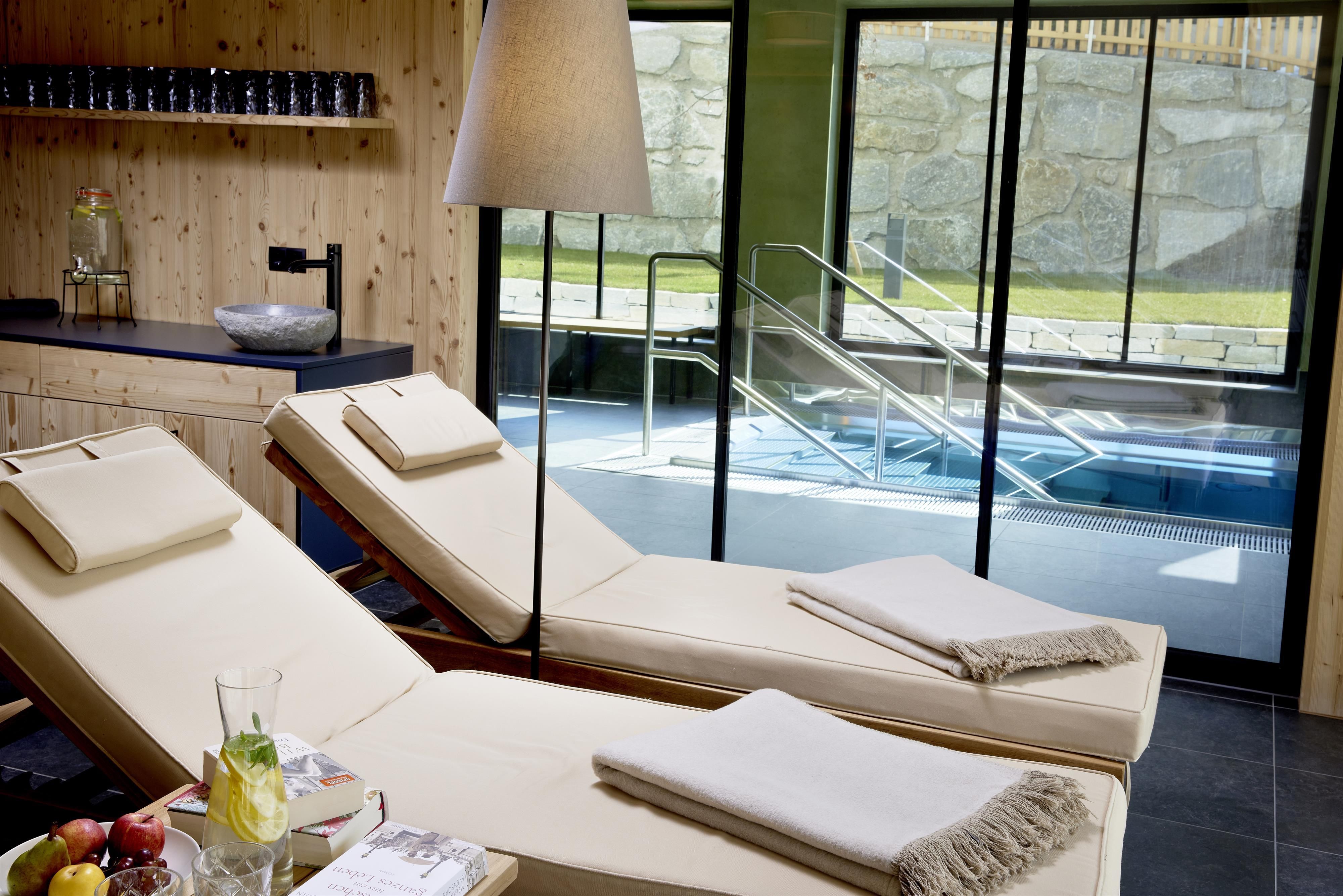 A modern wellness area with comfortable lounges and a large window view of a hot tub. Fresh fruit and a drink complete the relaxing atmosphere.
