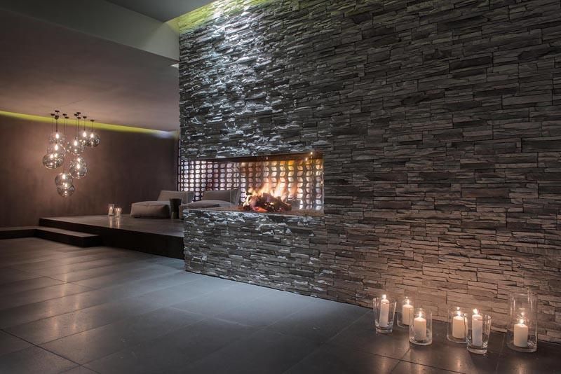 An elegant room with a stone wall and a cozy fireplace. Soft light from candles complements the relaxing atmosphere.
