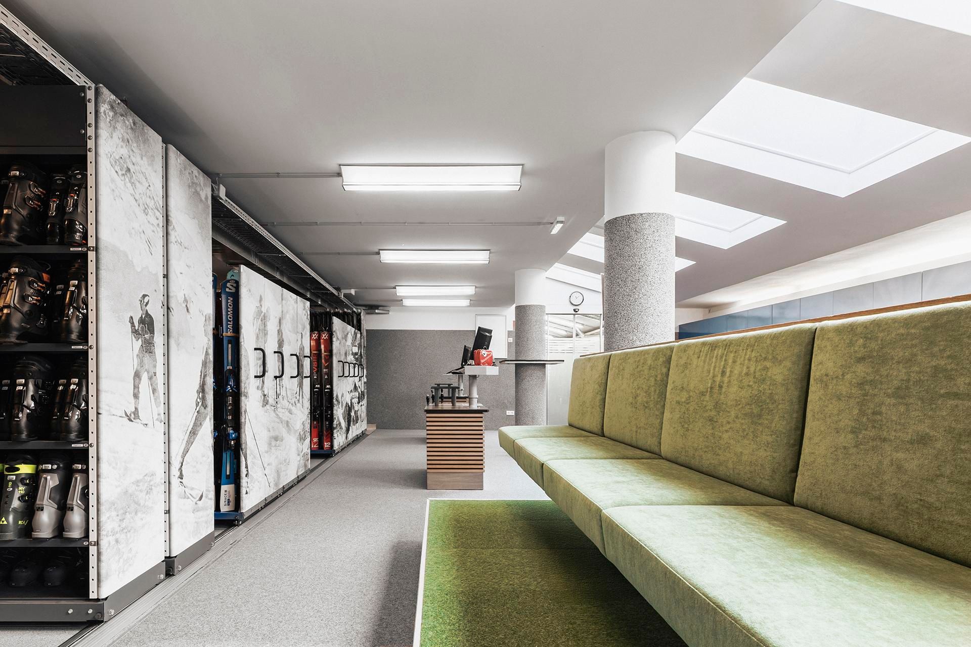 A modern space with a green seating area and large windows. In the background, lockers and a reception desk are visible.