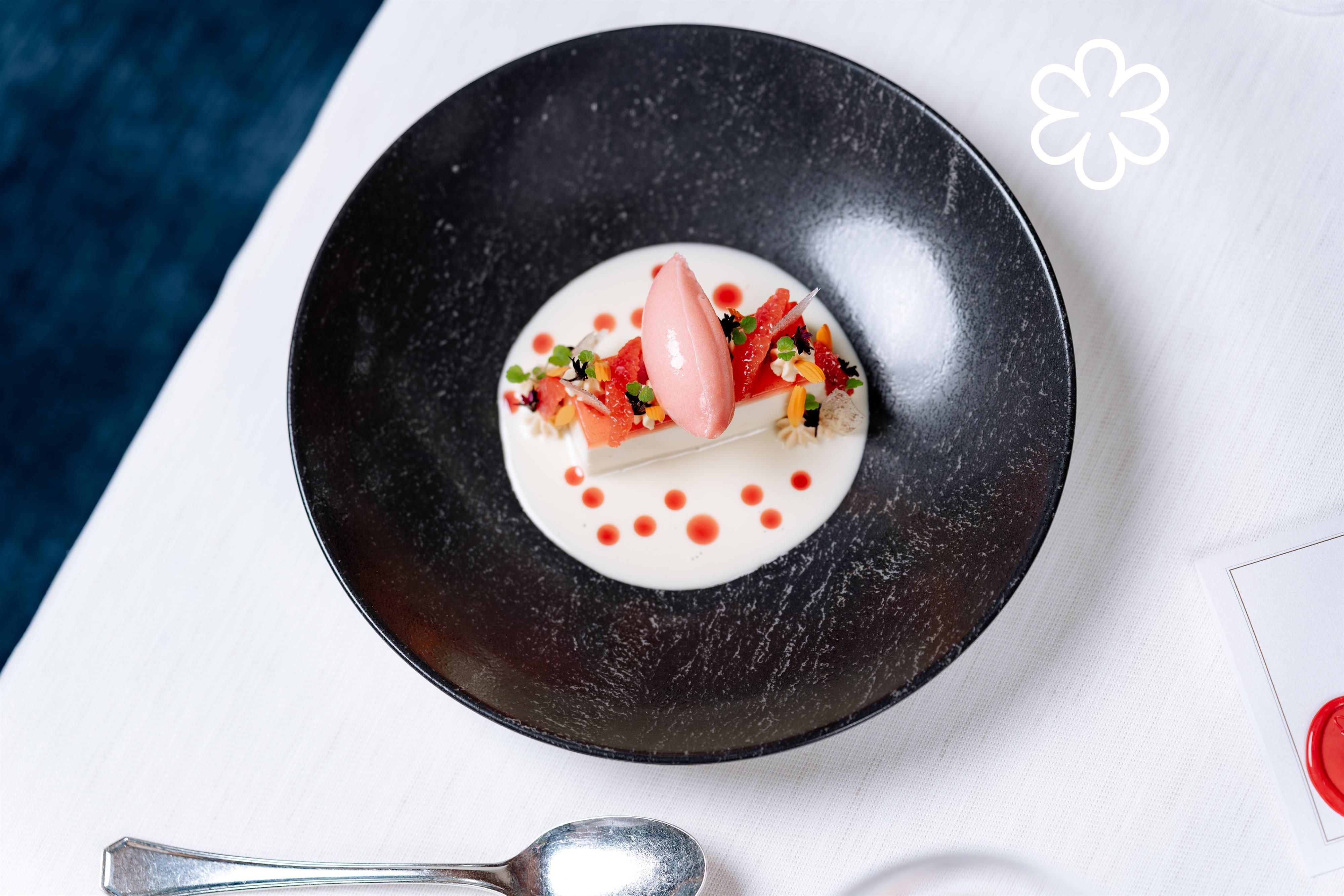 An artfully arranged dessert on a black plate. The dessert features a light cream, fresh berries, and a pink scoop of ice cream.