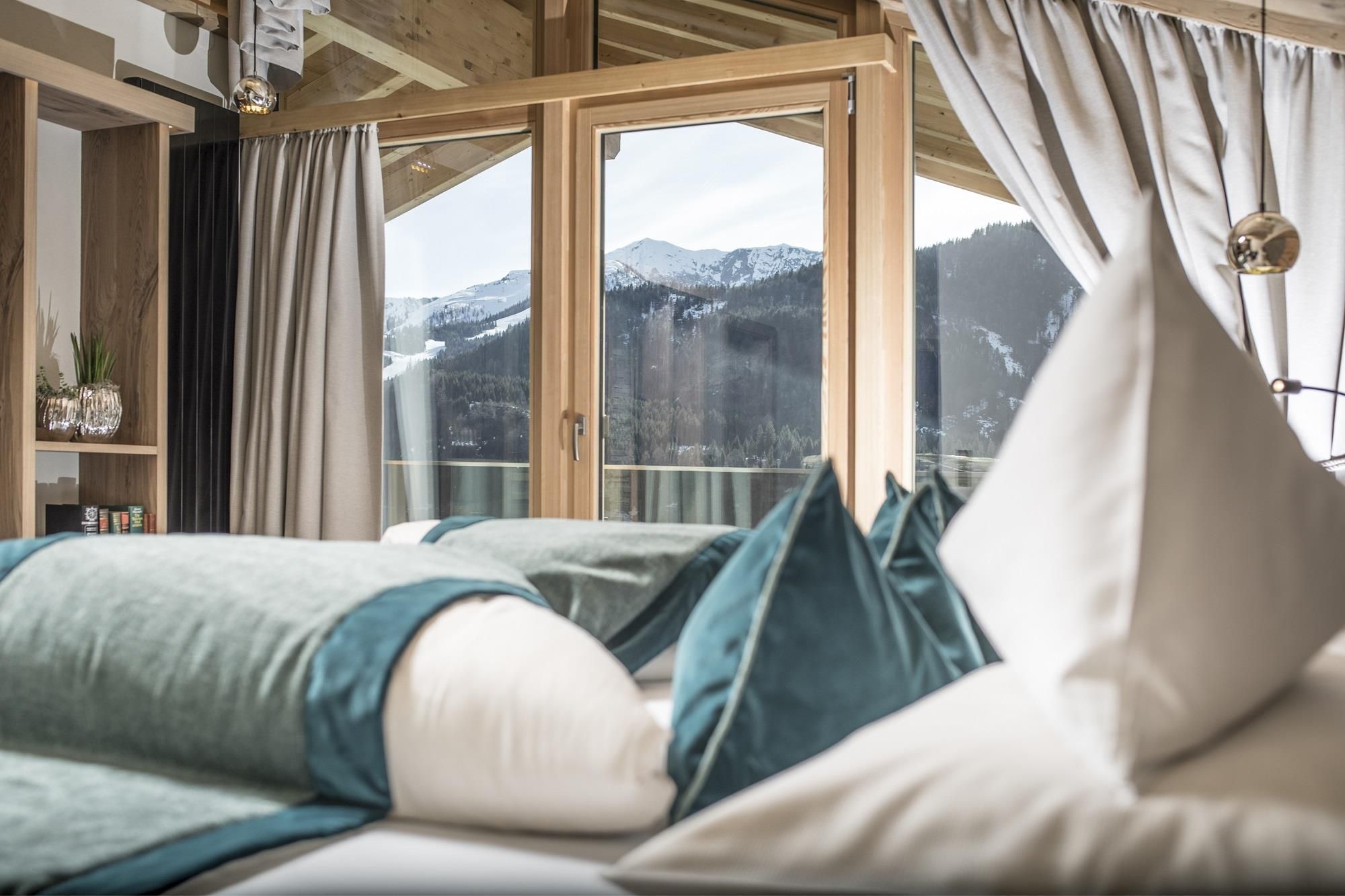 An elegant room with a large window that shows a beautiful mountain landscape. The decor is modern and cozy, with cushions in soft colors.