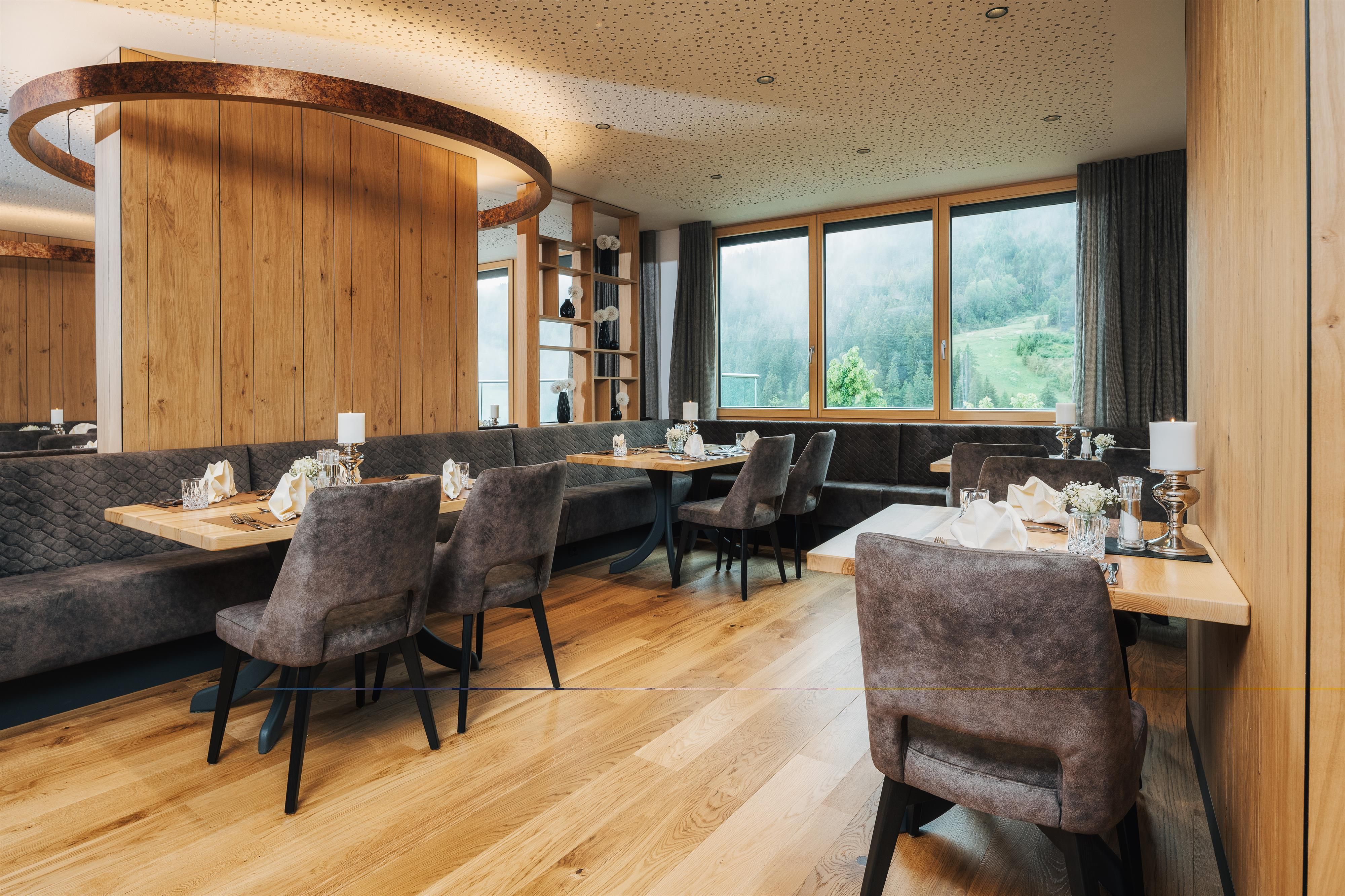An elegant restaurant with wooden decor and large windows. The tables are beautifully set and offer a view of the greenery.