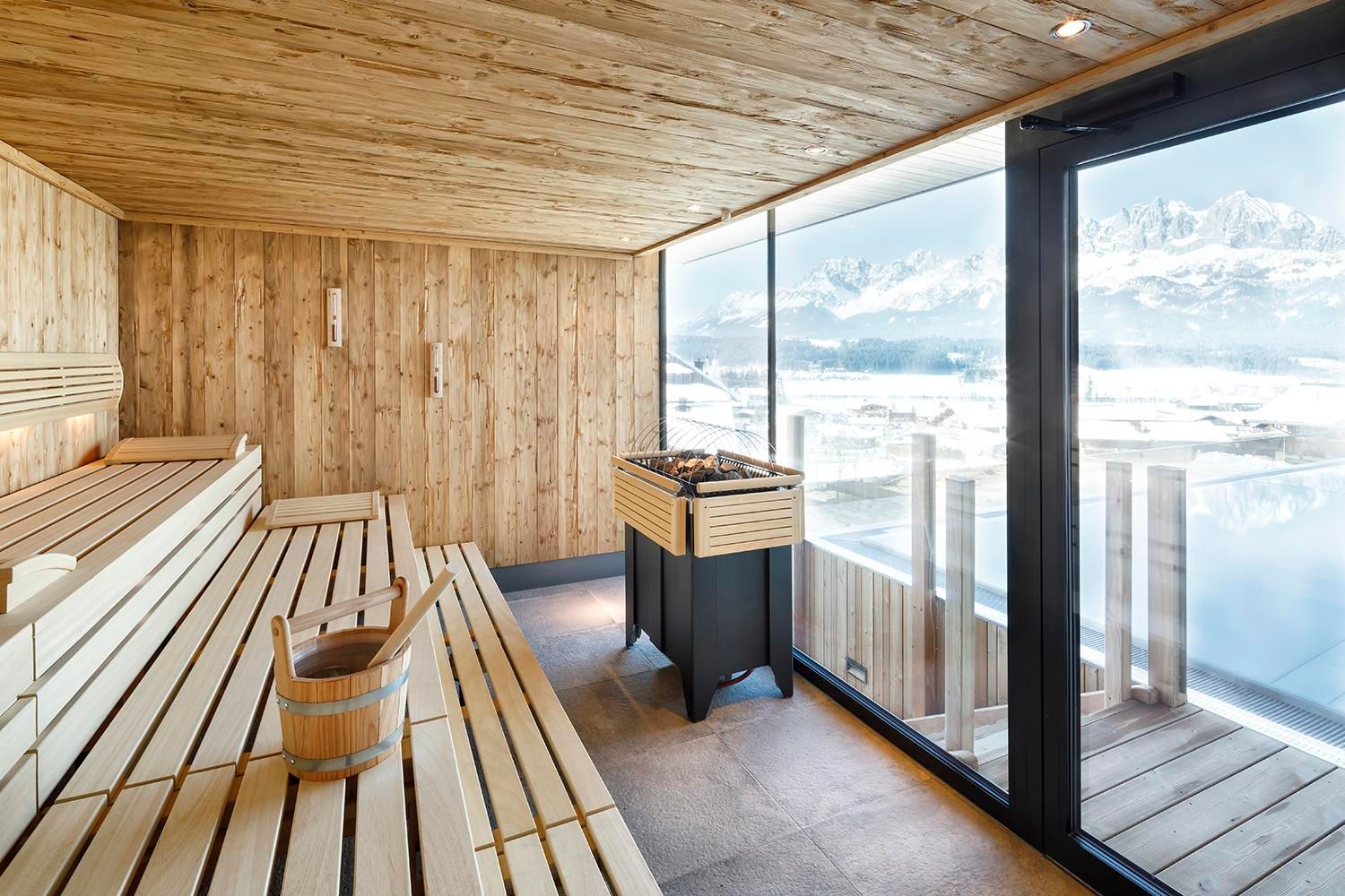 A modern sauna interior made of light wood with a window overlooking the mountains. The sauna is minimally furnished and radiates tranquility.