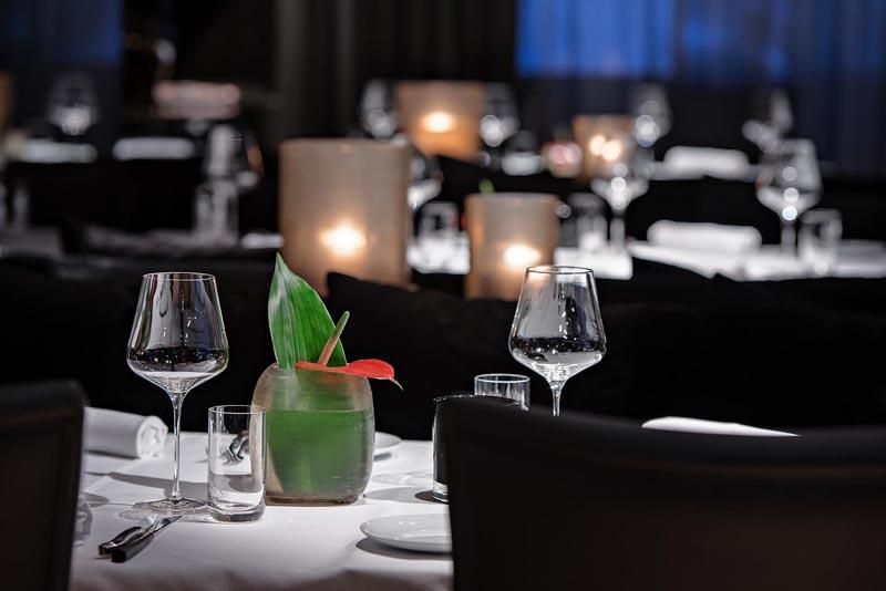 An elegant restaurant with beautifully set tables. Glasses and a decorative plant create an inviting atmosphere.