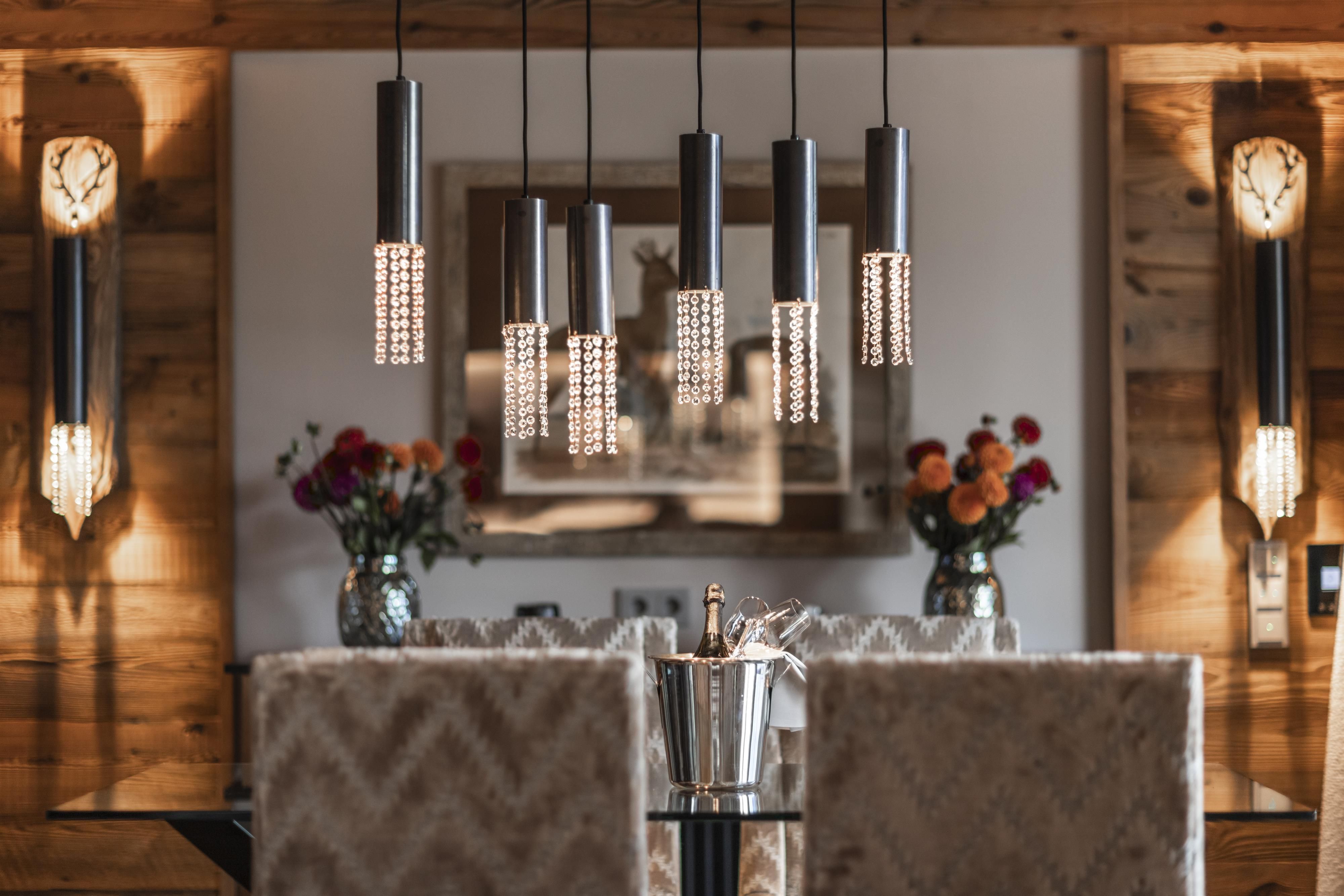 A stylish dining room with elegant pendant lights and cozy chairs. Vases with colorful flowers create an inviting atmosphere.
