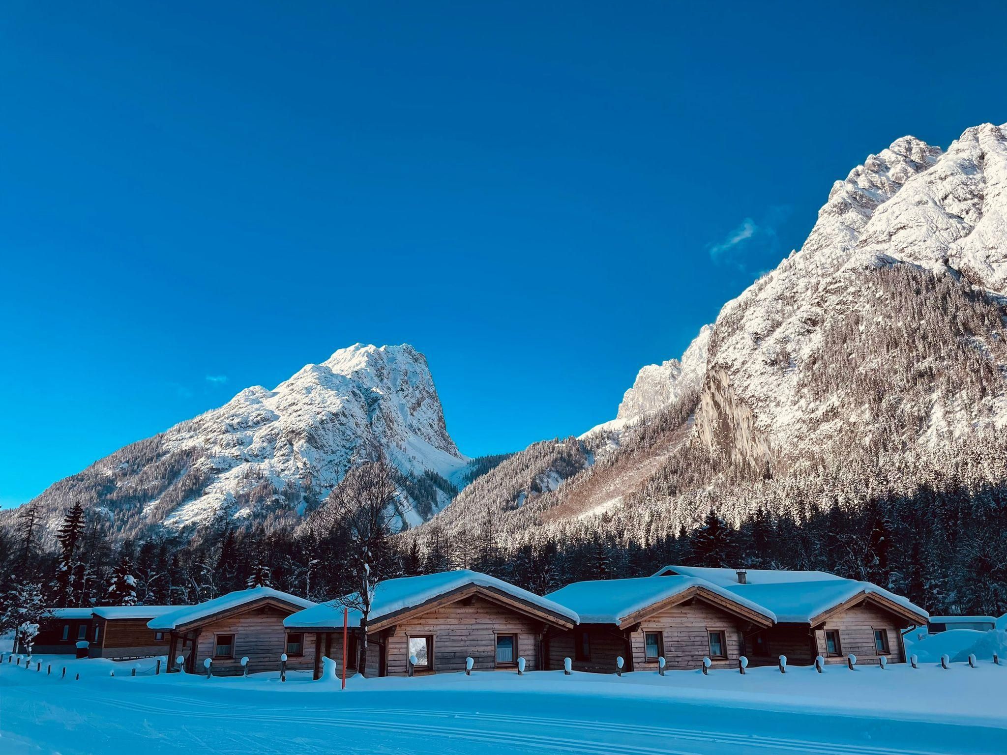 A picturesque winter landscape with snow-covered huts and majestic mountains in the background. The clear blue sky invites dreaming.