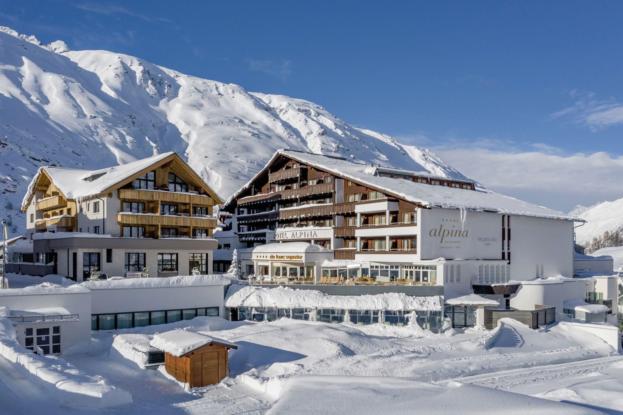 A modern hotel amidst a snowy mountain landscape. The buildings are surrounded by snow and the sky is clear and blue.