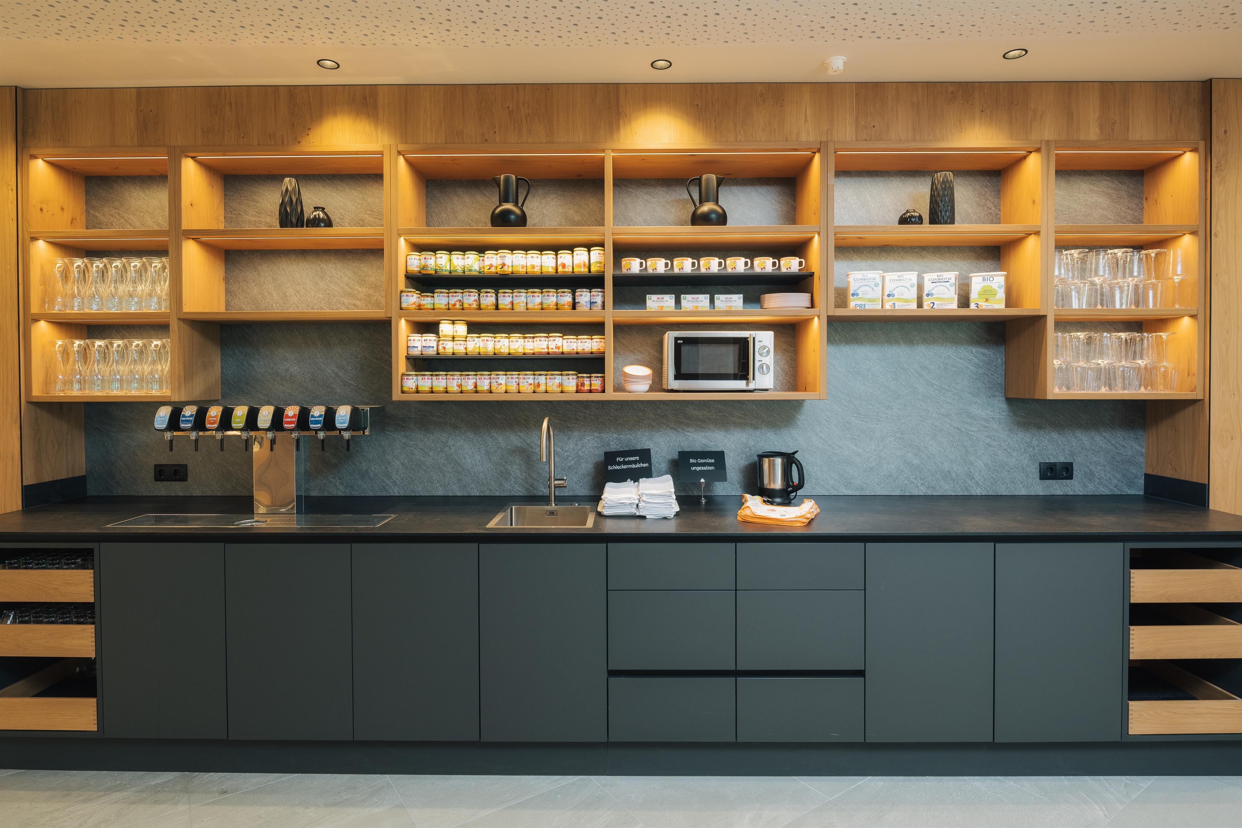A modern kitchen unit with open shelves and a variety of teas. The equipment includes a kettle, a microwave, and elegant glasses.