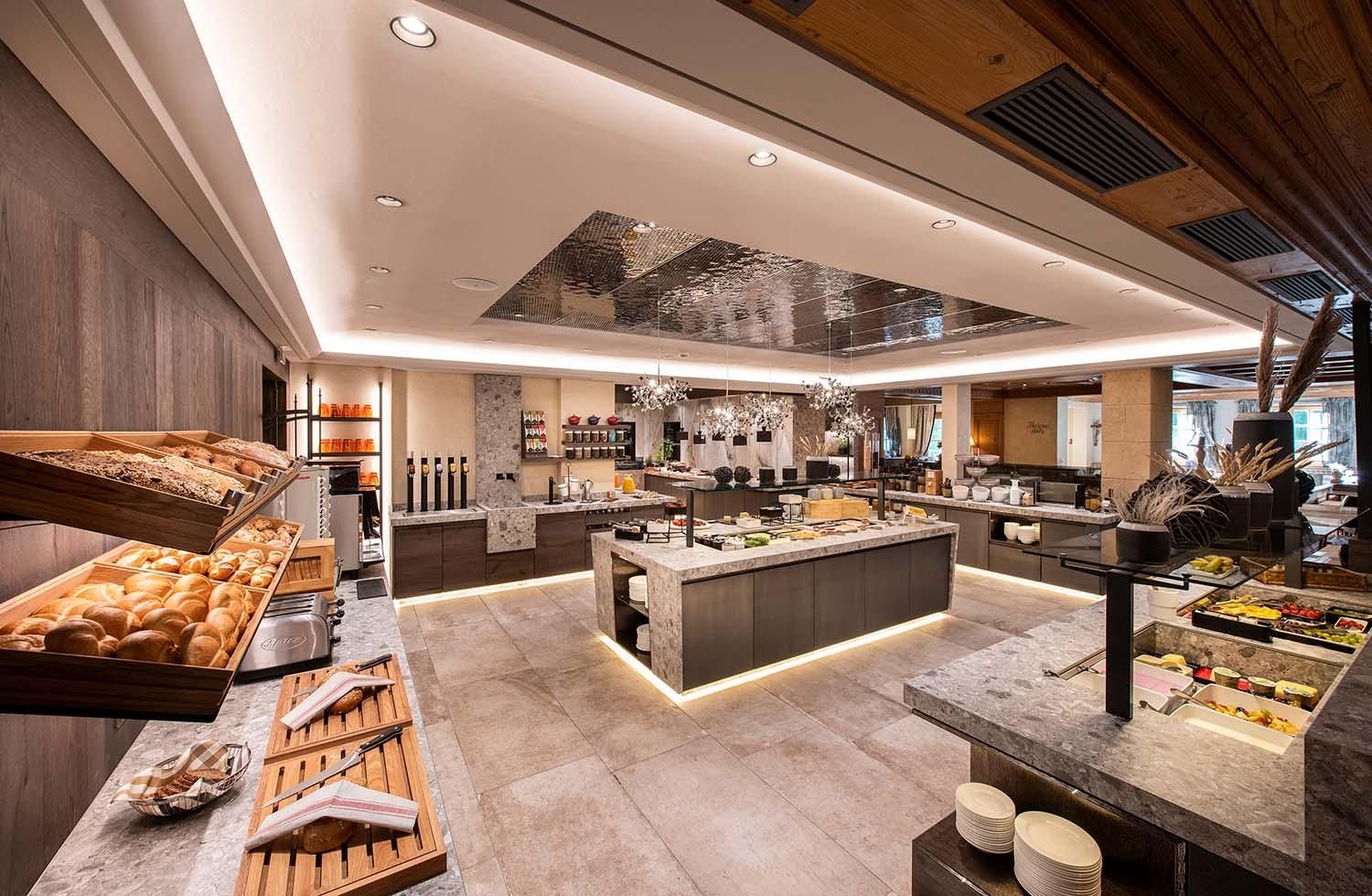 A modern restaurant with a generous buffet. There is a selection of fresh rolls, fruits, and other dishes in an elegantly decorated room.