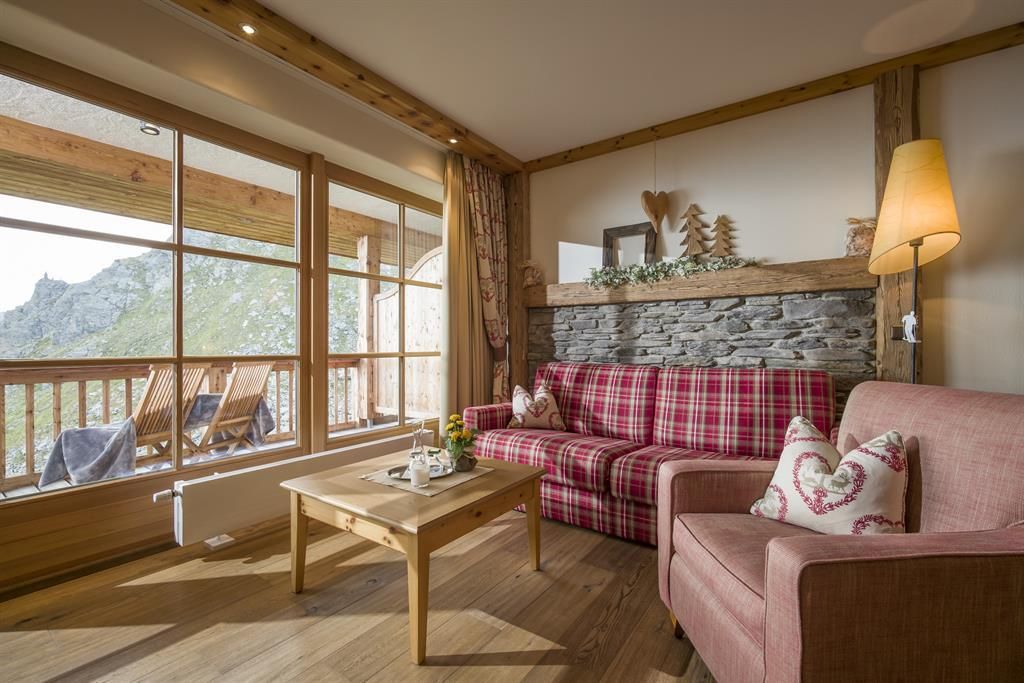 A cozy living room with a checkered sofa and a harmonious wooden touch. Large windows offer a view of the mountain landscape.