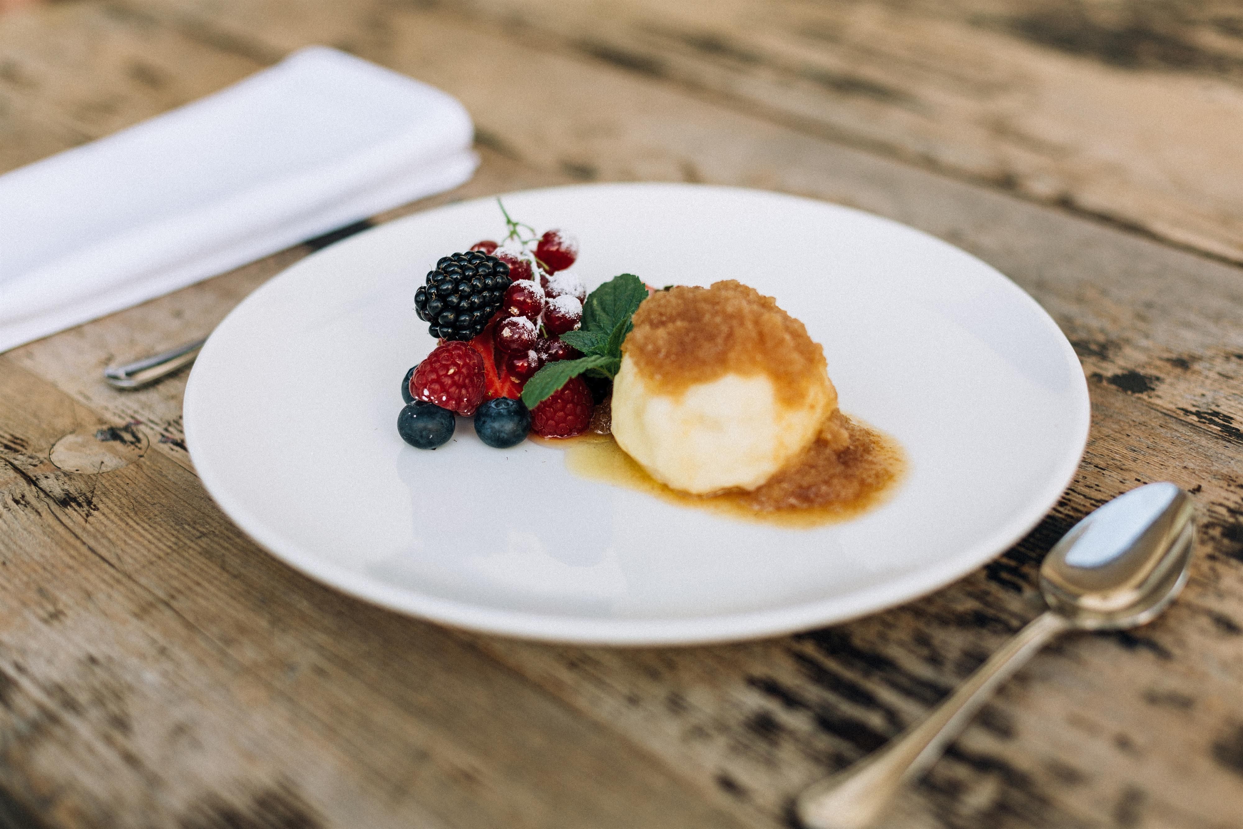 A delicious dessert with a scoop of ice cream, garnished with fresh berries and some caramel sauce. The dish is placed on a white plate and set on a rustic wooden table.