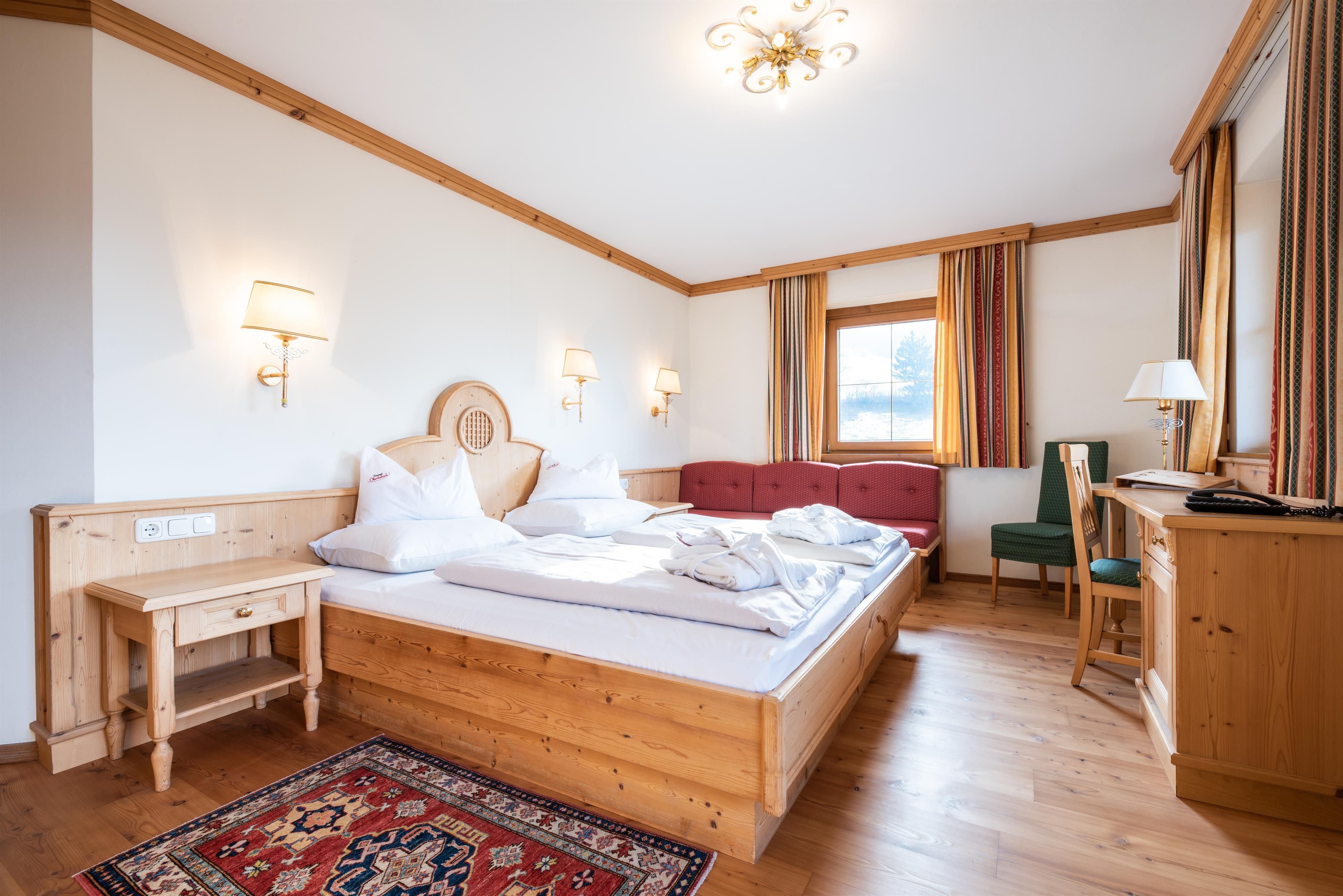 A cozy bedroom with a large bed and wooden paneling. There are additional seating options and a rug on the floor.