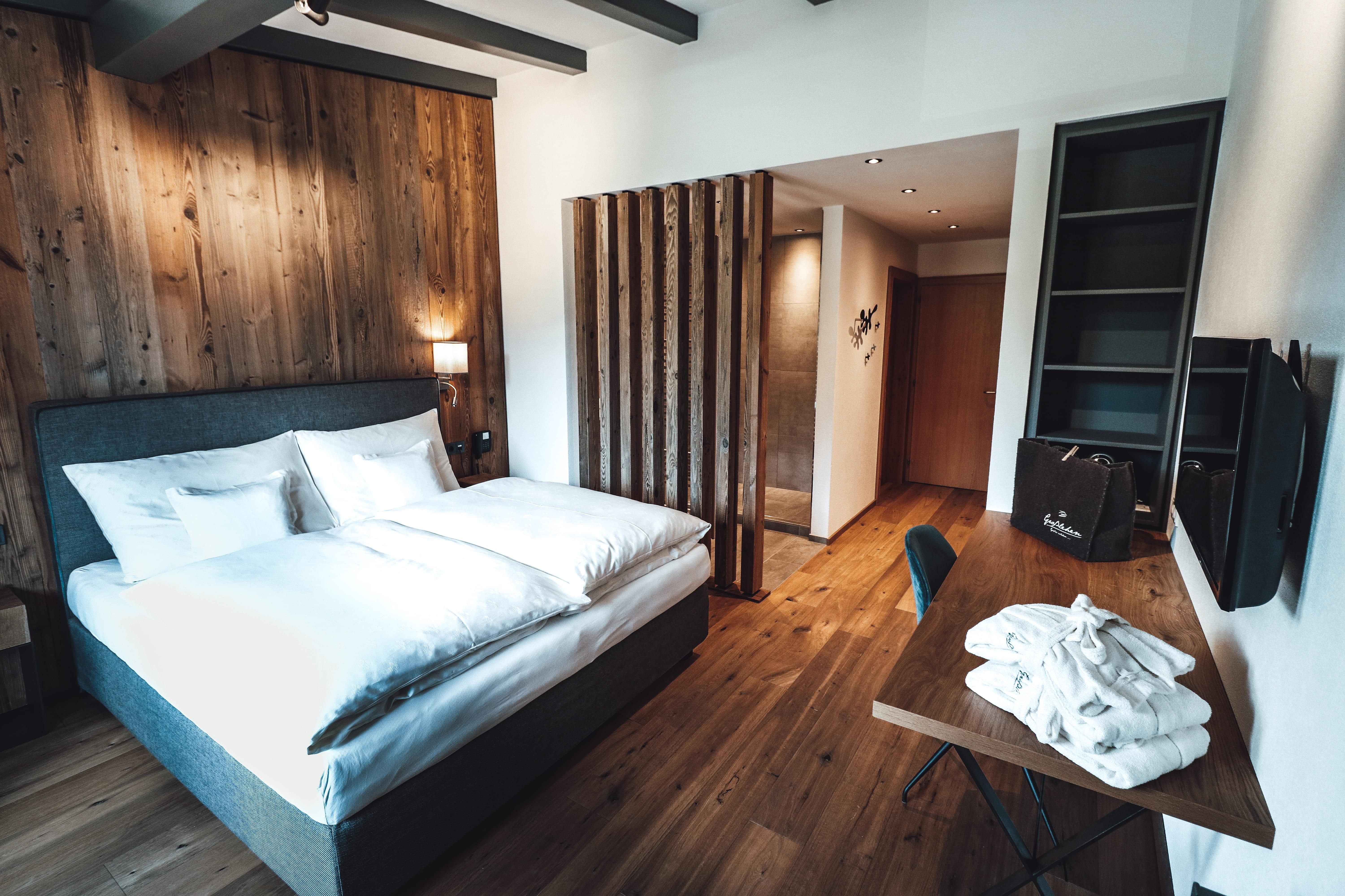 A modern room with a large bed and wooden details. There is a table and a television, as well as a separate area for the bathroom.