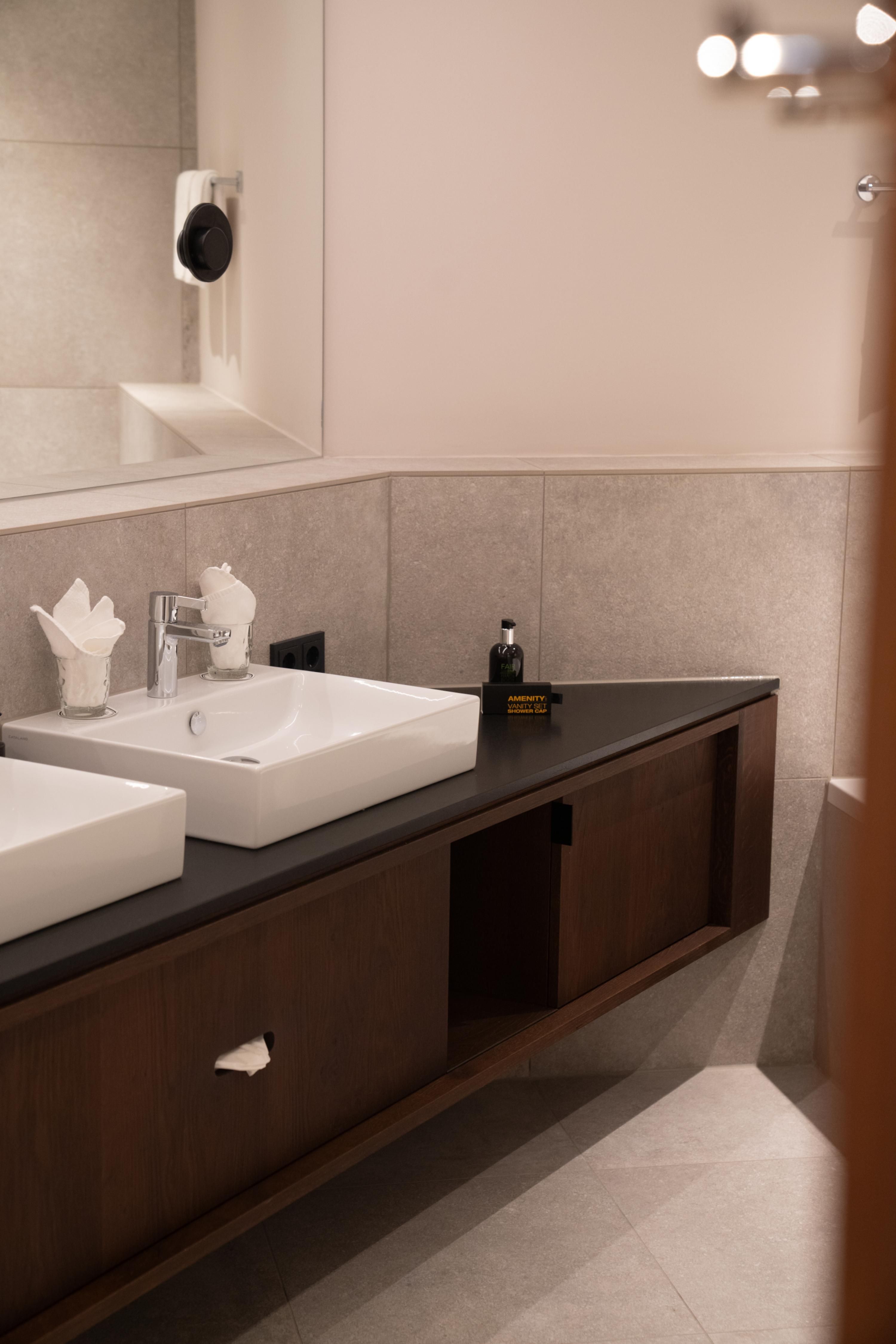 A modern bathroom with double sinks and an elegant wooden cabinet. The walls are in neutral colors, and there is subtle lighting.