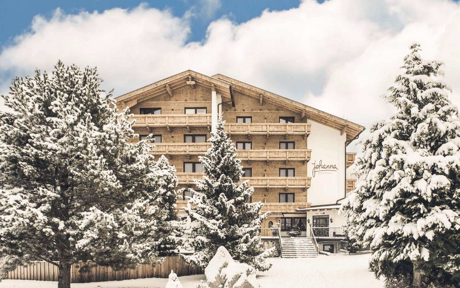 A luxurious hotel surrounded by snow-covered trees in a wintry landscape. The sky is blue with some clouds.