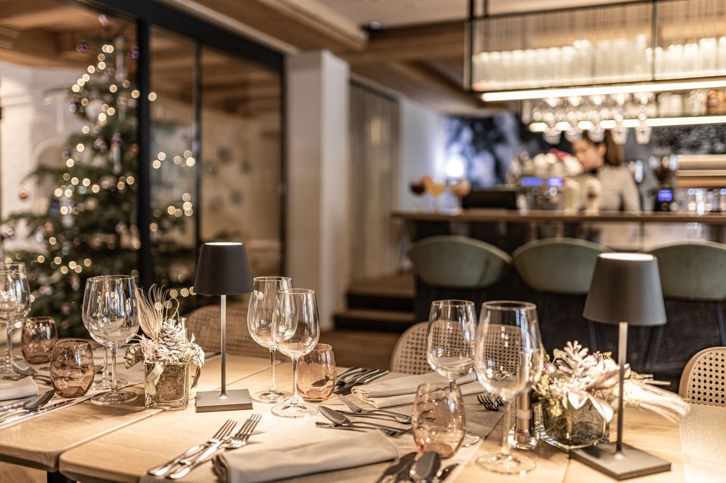An elegantly set table in a stylish restaurant. In the background, a decorated Christmas tree and the bar are visible.
