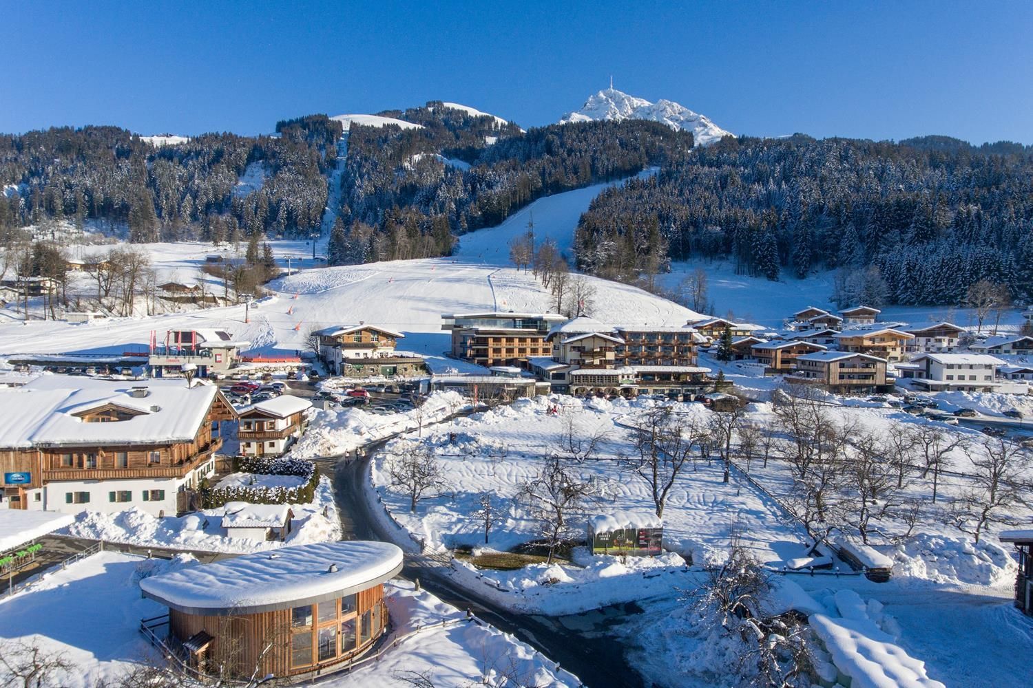 A picturesque winter landscape with snow-covered mountains and charming chalets. The sky is clear and blue, while the landscape appears calm and idyllic.