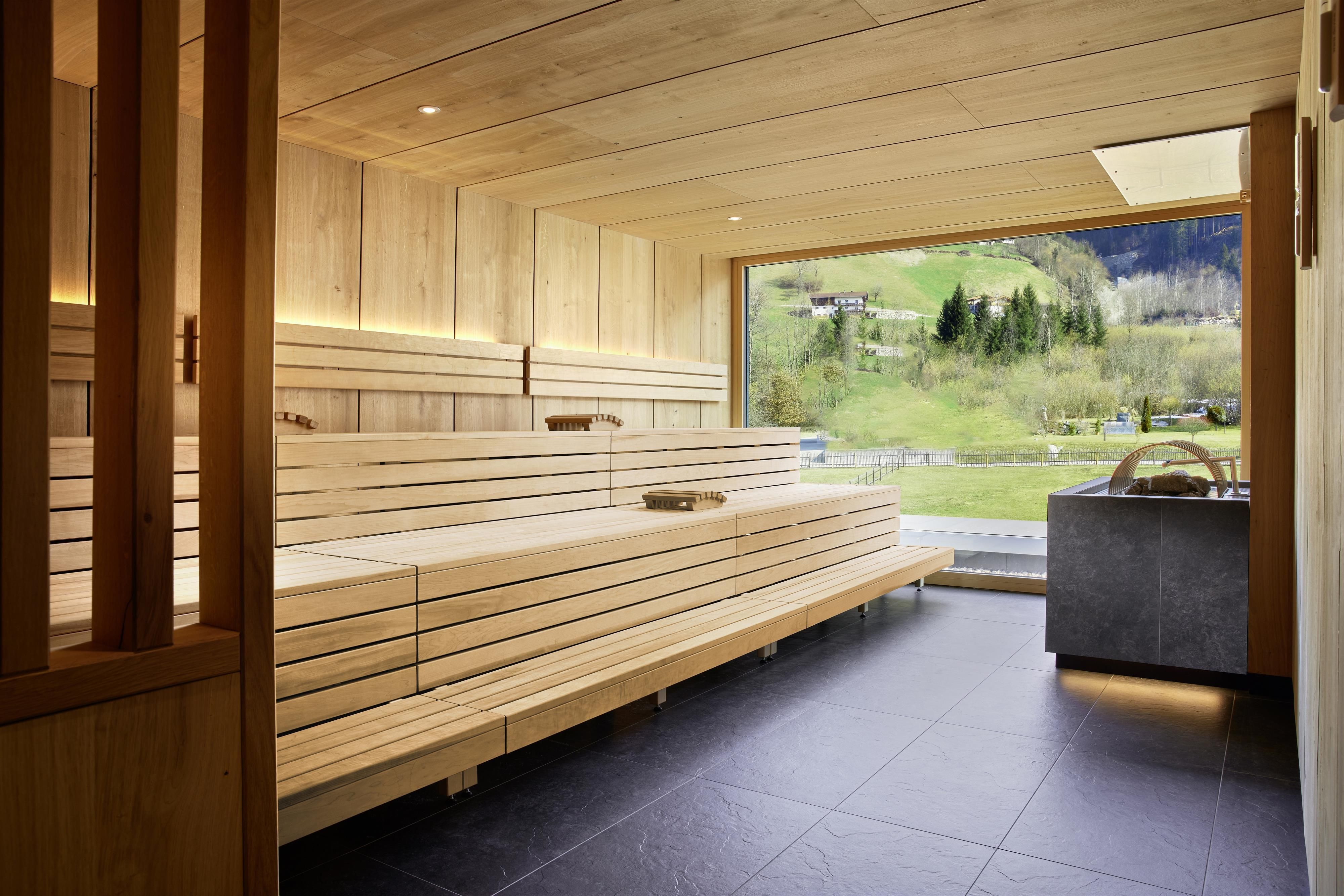 A modern wellness area with bright wooden paneling and a large window front that offers a view of the green landscape. The benches are continuous and invite relaxation.