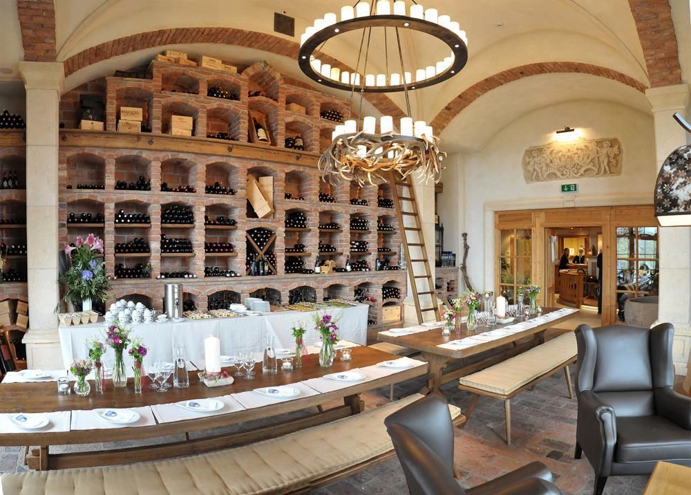 A stylish restaurant with a wall of wine shelves and a long table. The decor is cozy and inviting, perfect for dinners.