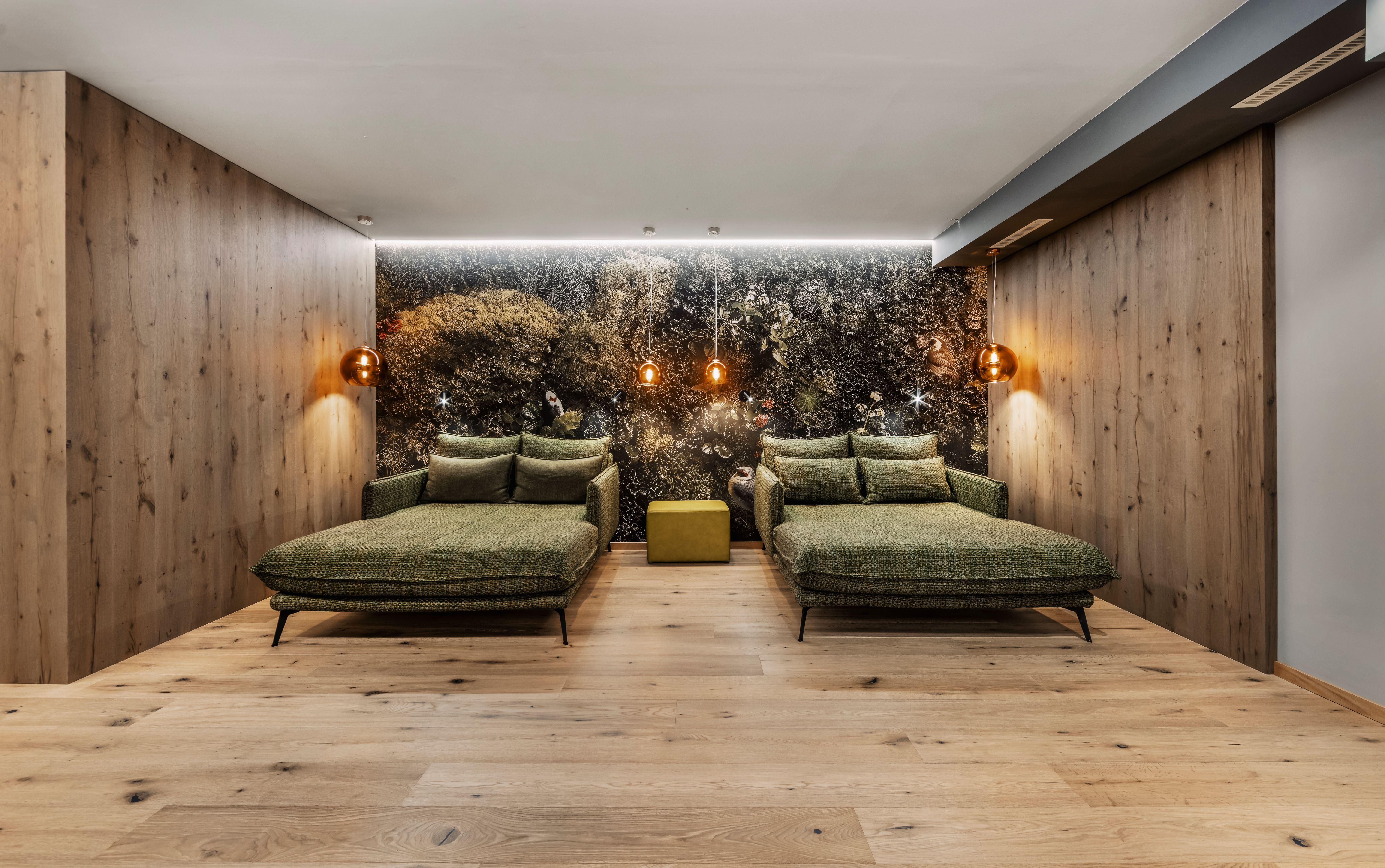 A modern relaxation room with two green loungers and warm wooden details. The wall is decorated with a naturalistic planting, creating a calming atmosphere.