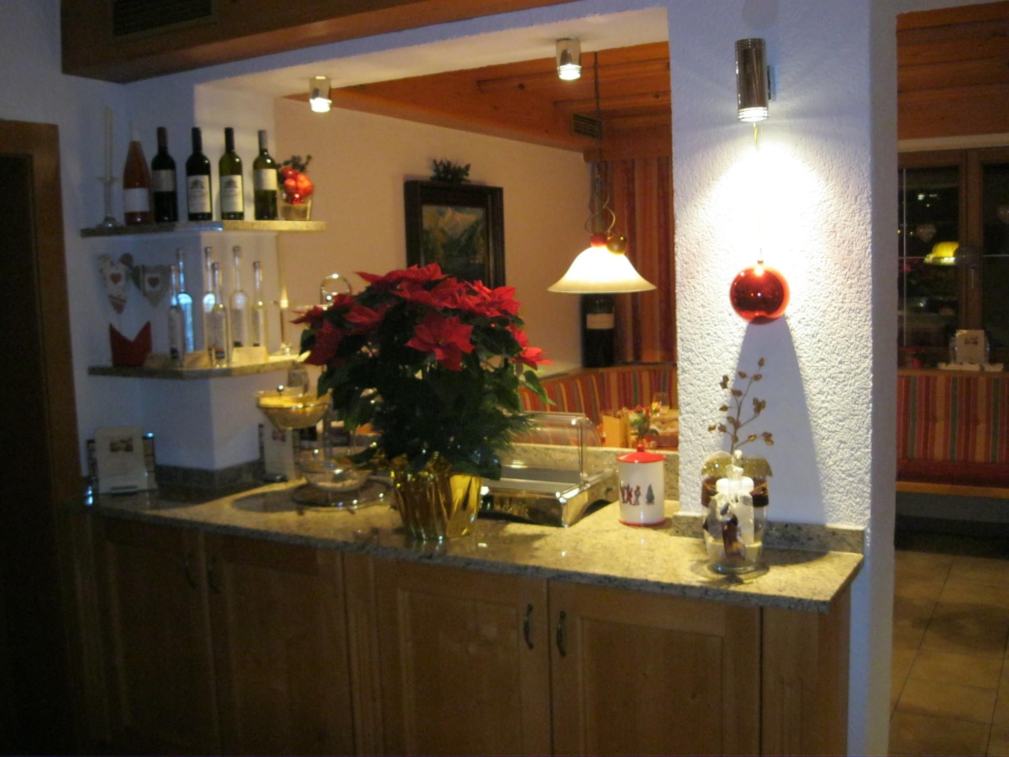 A cozy room with a wooden counter and a pretty Christmas decoration. On the counter, there is a pot with Christmas stars, and in the background, wines and glasses are visible.
